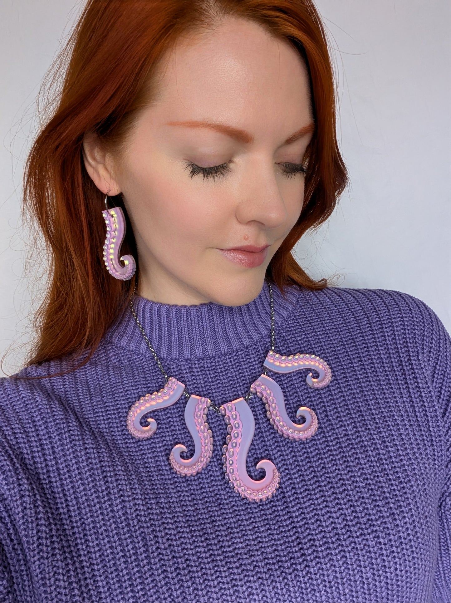 Woman wearing a purple sweater with pink octopus designs and matching earrings.