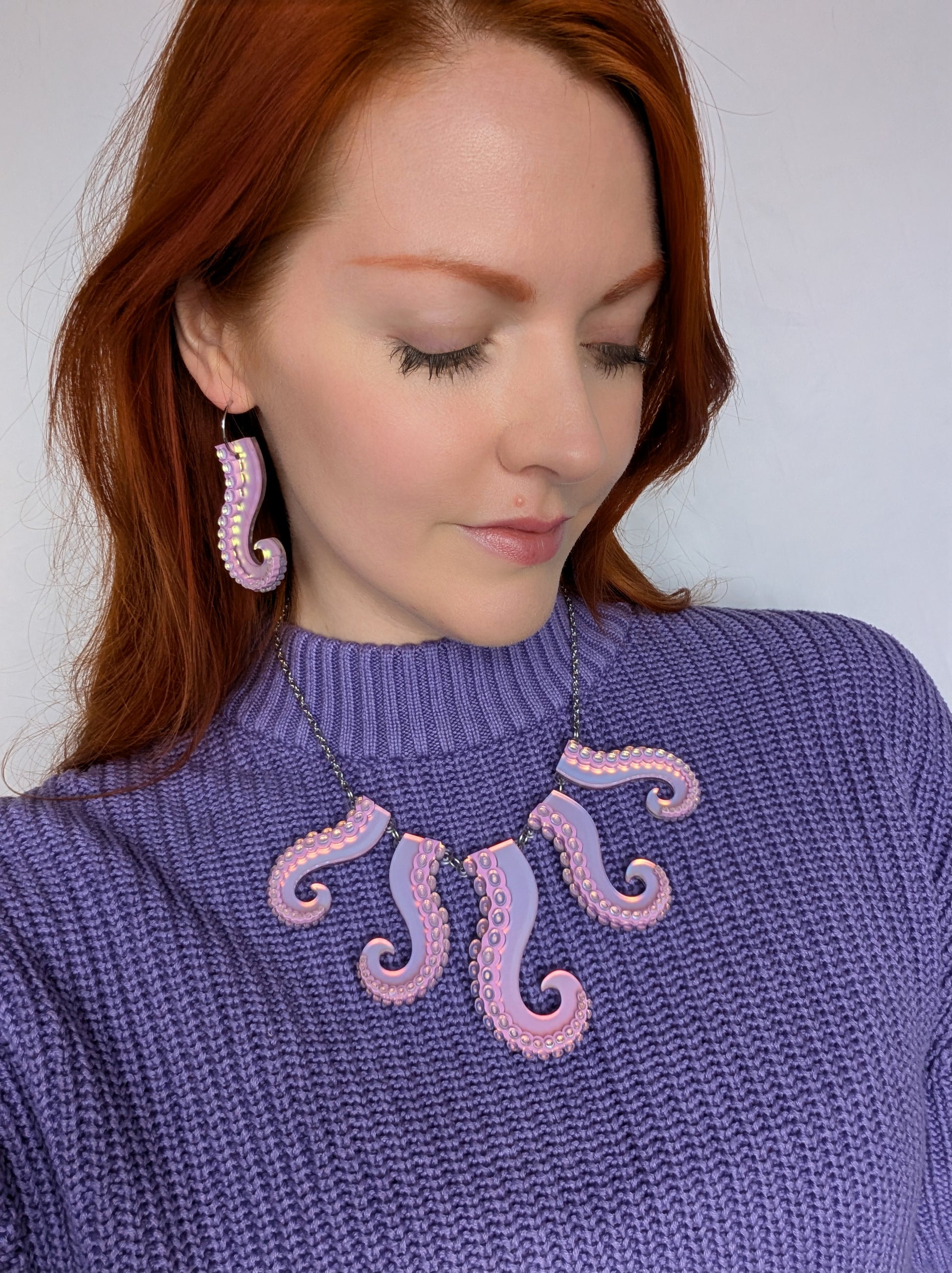 Woman wearing a purple sweater with pink octopus designs and matching earrings.