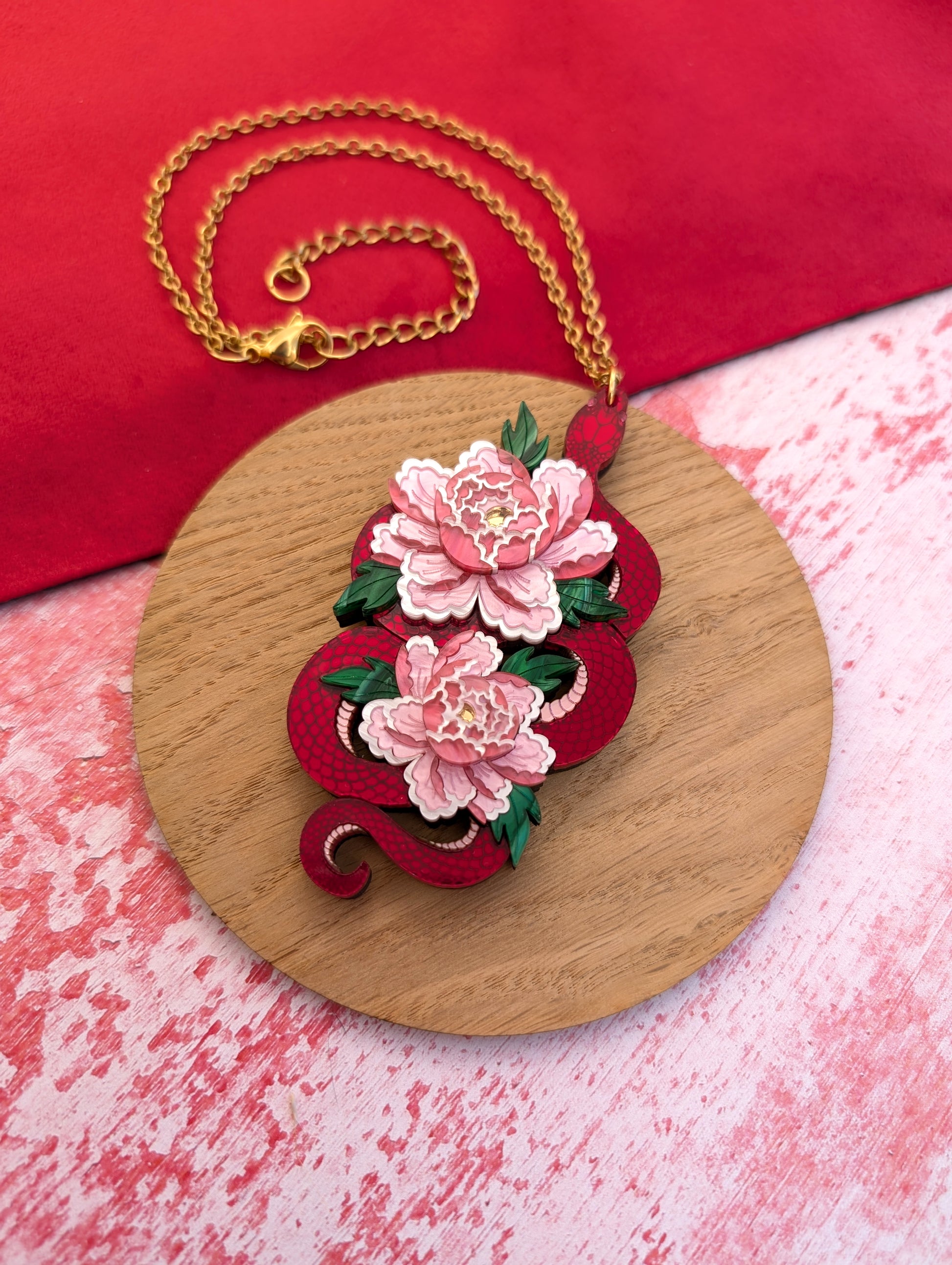 A statement pendant featuring a red snake with peony flowers, displayed on a wooden round stand.
