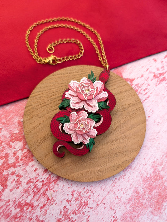 A statement pendant featuring a red snake with peony flowers, displayed on a wooden round stand.