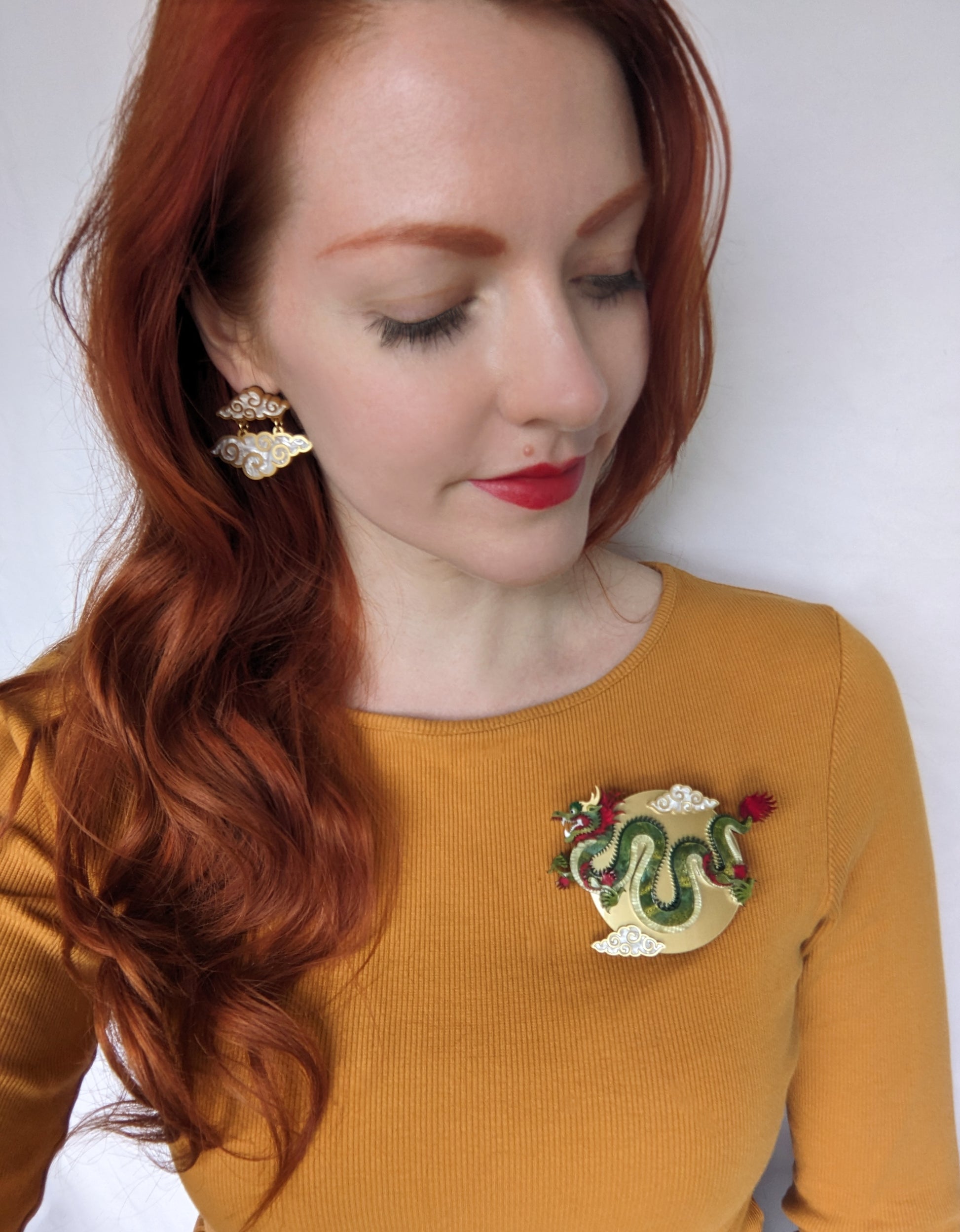 A large, colorful brooch or necklace featuring a detailed Chinese dragon design with green, red, and yellow elements, displayed against a gold and red background.