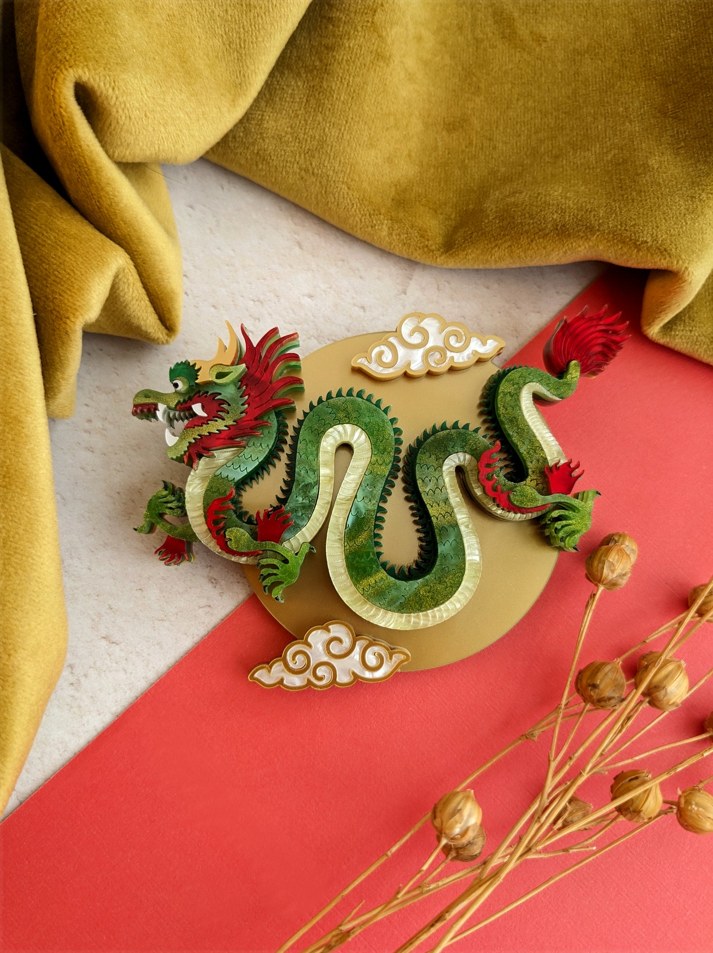 A striking green and gold Chinese dragon brooch or necklace with intricate details and metallic accents, displayed against a red and yellow background.