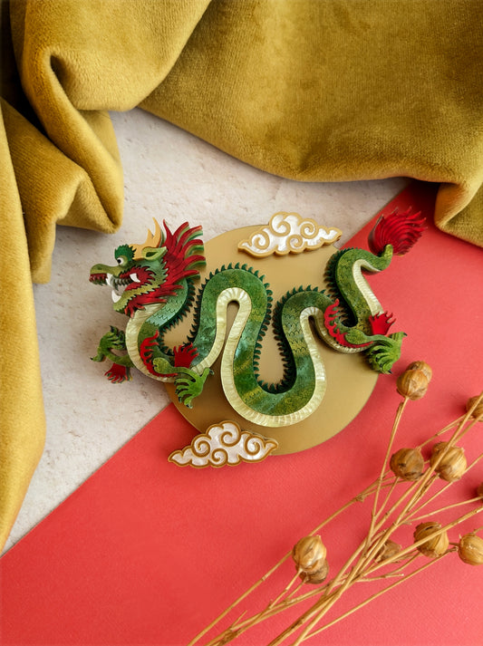 A striking green and gold Chinese dragon brooch or necklace with intricate details and metallic accents, displayed against a red and yellow background.