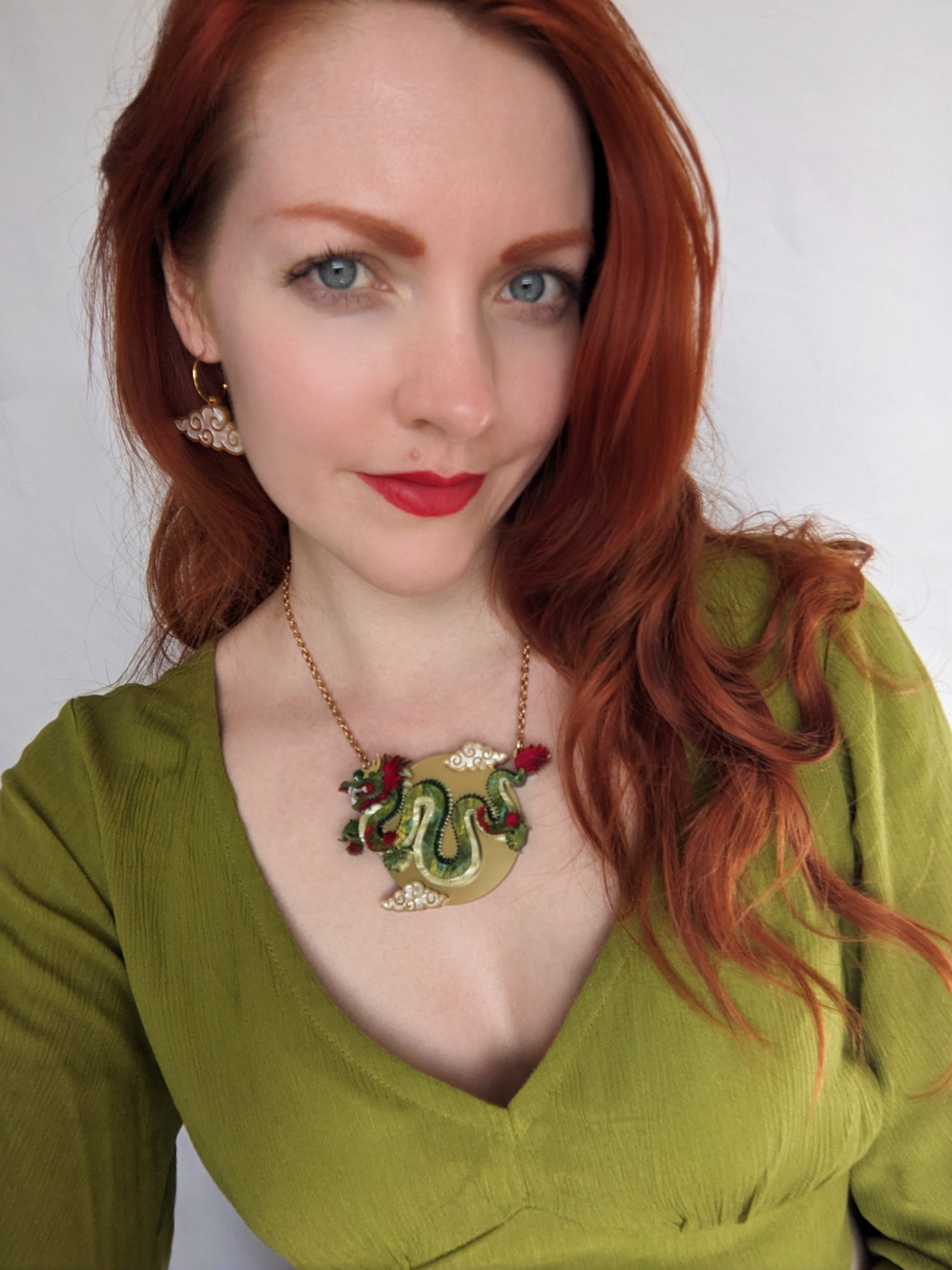 A large, colorful laser cut acrylic brooch or necklace featuring a detailed Chinese dragon design with green, red, and yellow elements, displayed against a gold and red background.