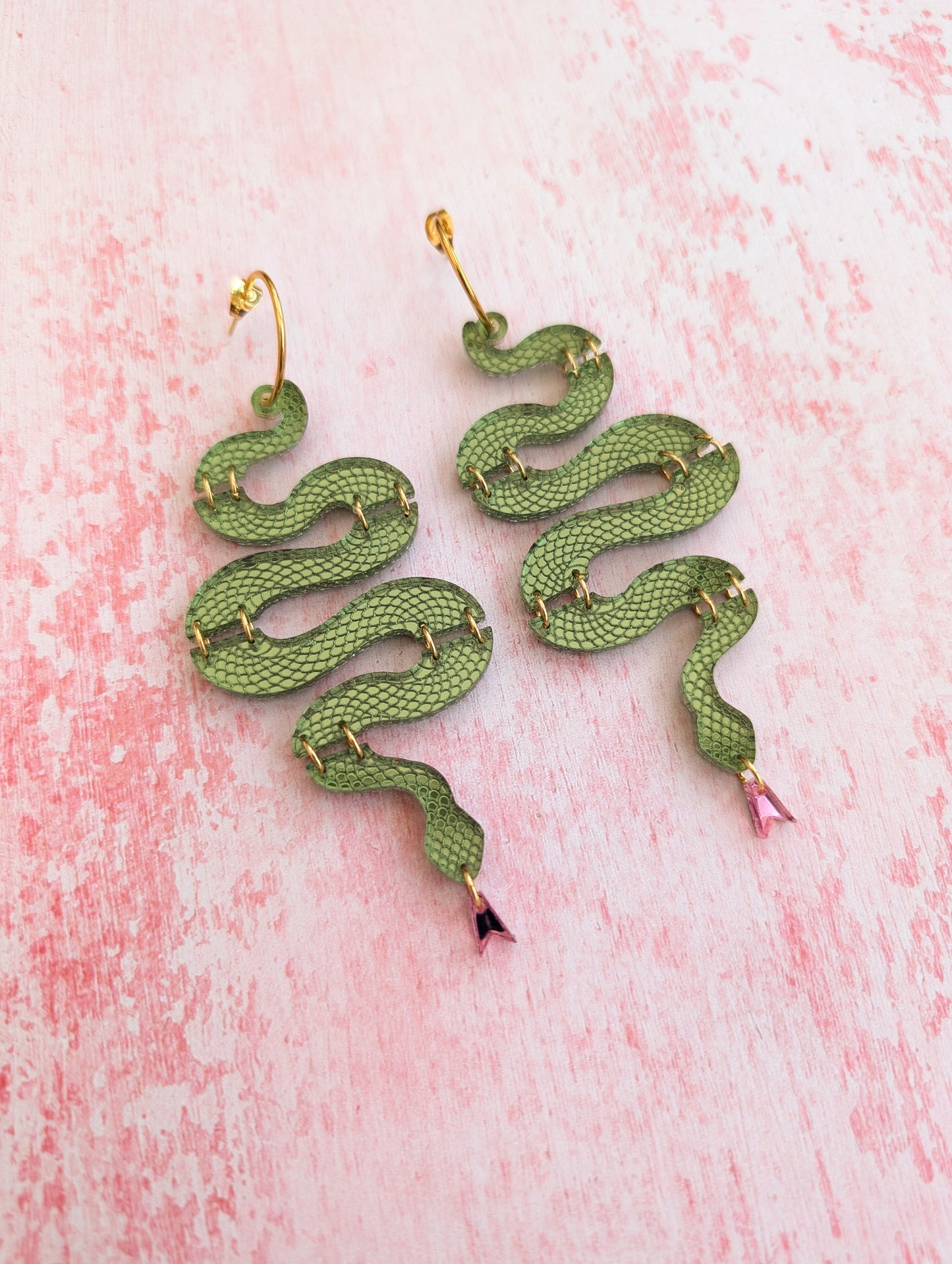 Green snake-shaped earrings on a pink textured background