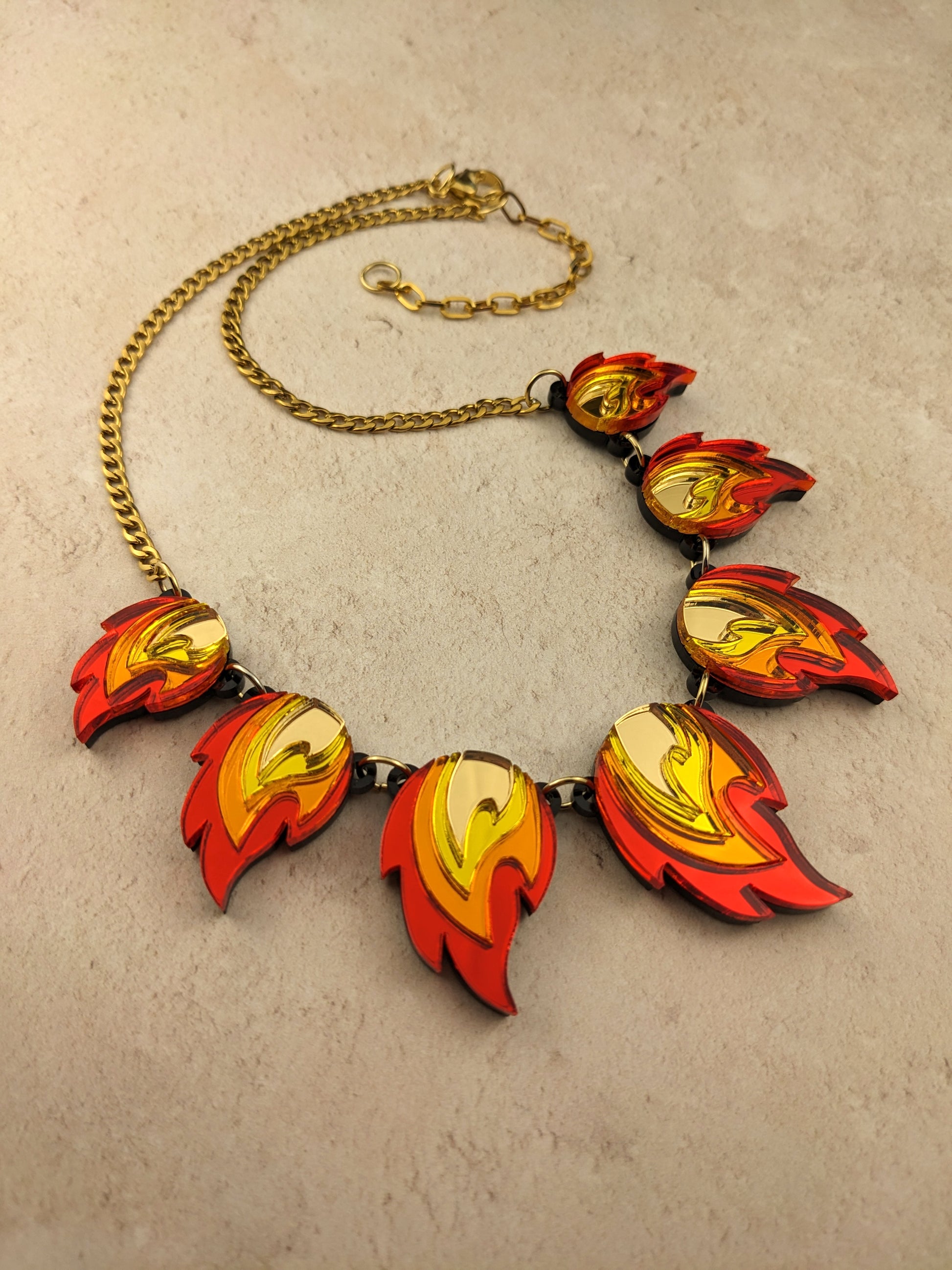A necklace with red, orange, yellow, and gold flame-shaped acrylic pendants, linked together with gold-plated jump rings on a gold-colored chain.