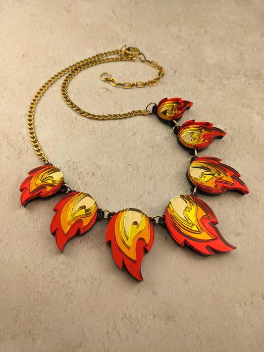 A necklace with red, orange, yellow, and gold flame-shaped acrylic pendants, linked together with gold-plated jump rings on a gold-colored chain.