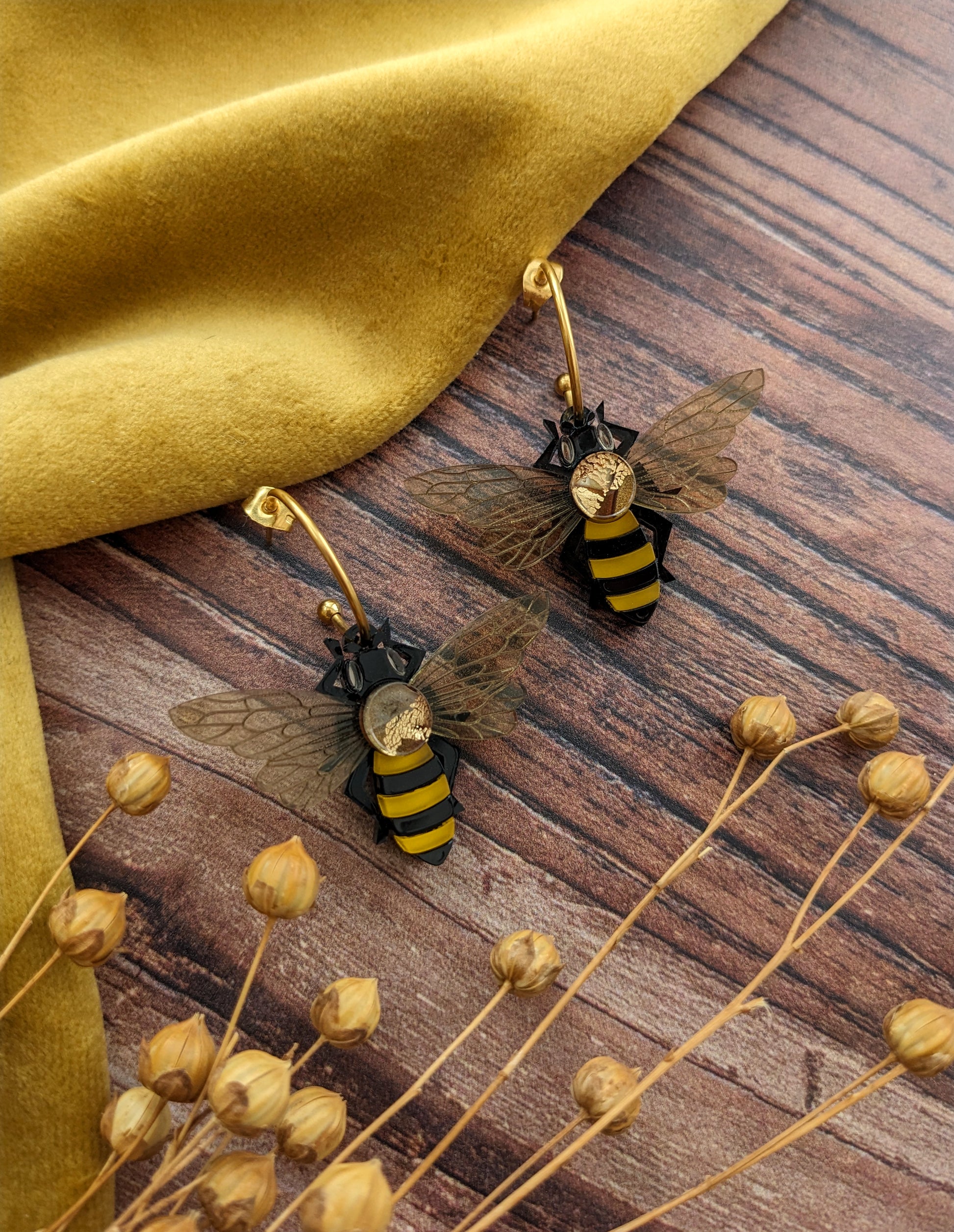 Bee-shaped earrings on a wooden surface with dried flowers