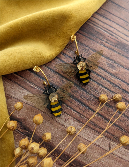Bee-shaped earrings on a wooden surface with dried flowers