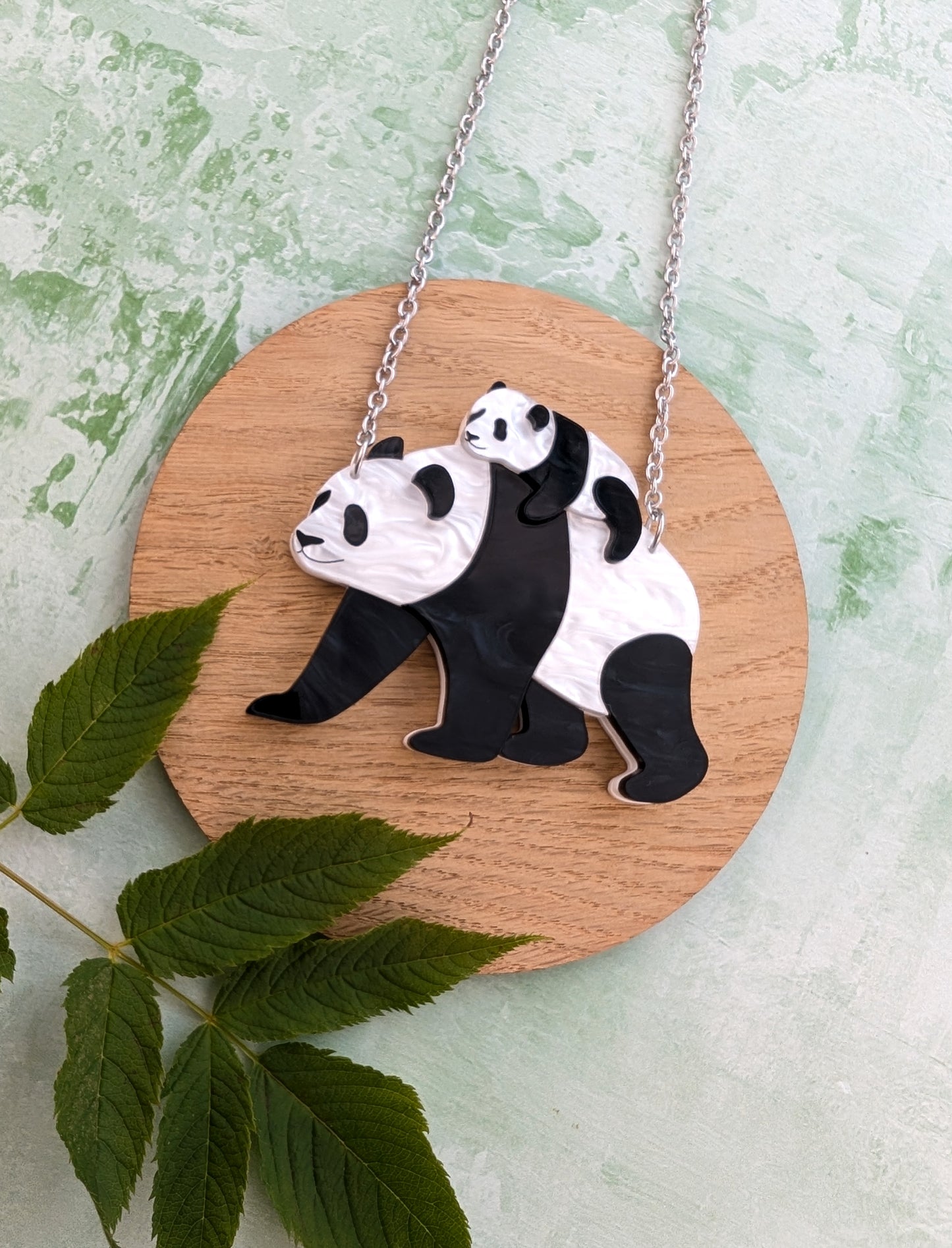 Pendant necklace with panda design on a wooden board with leaves