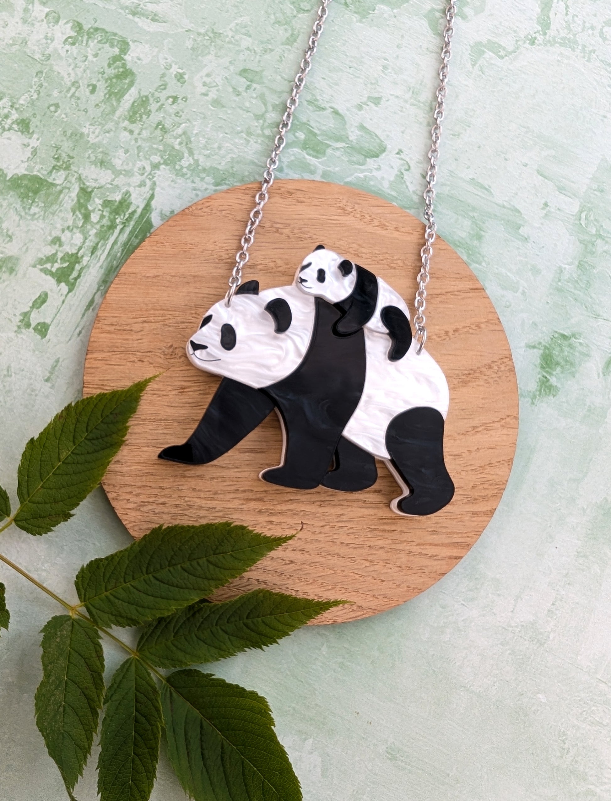 Pendant necklace with panda design on a wooden board with leaves