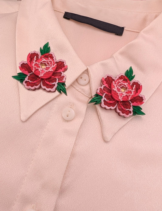 Two handmade acrylic floral brooches with red, pink, and green accents attached to a collar on a beige shirt