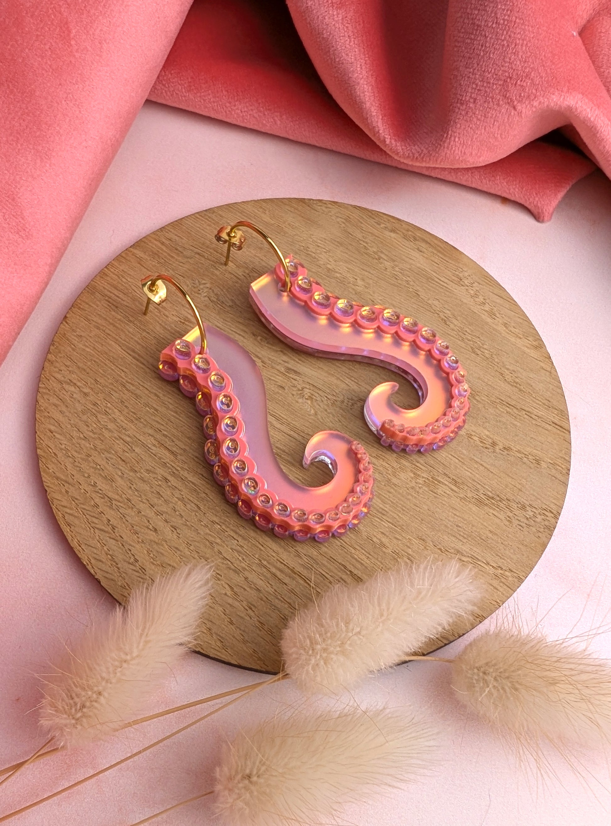 Pink and gold octopus tentacle earrings on a wooden stand with a pink fabric background