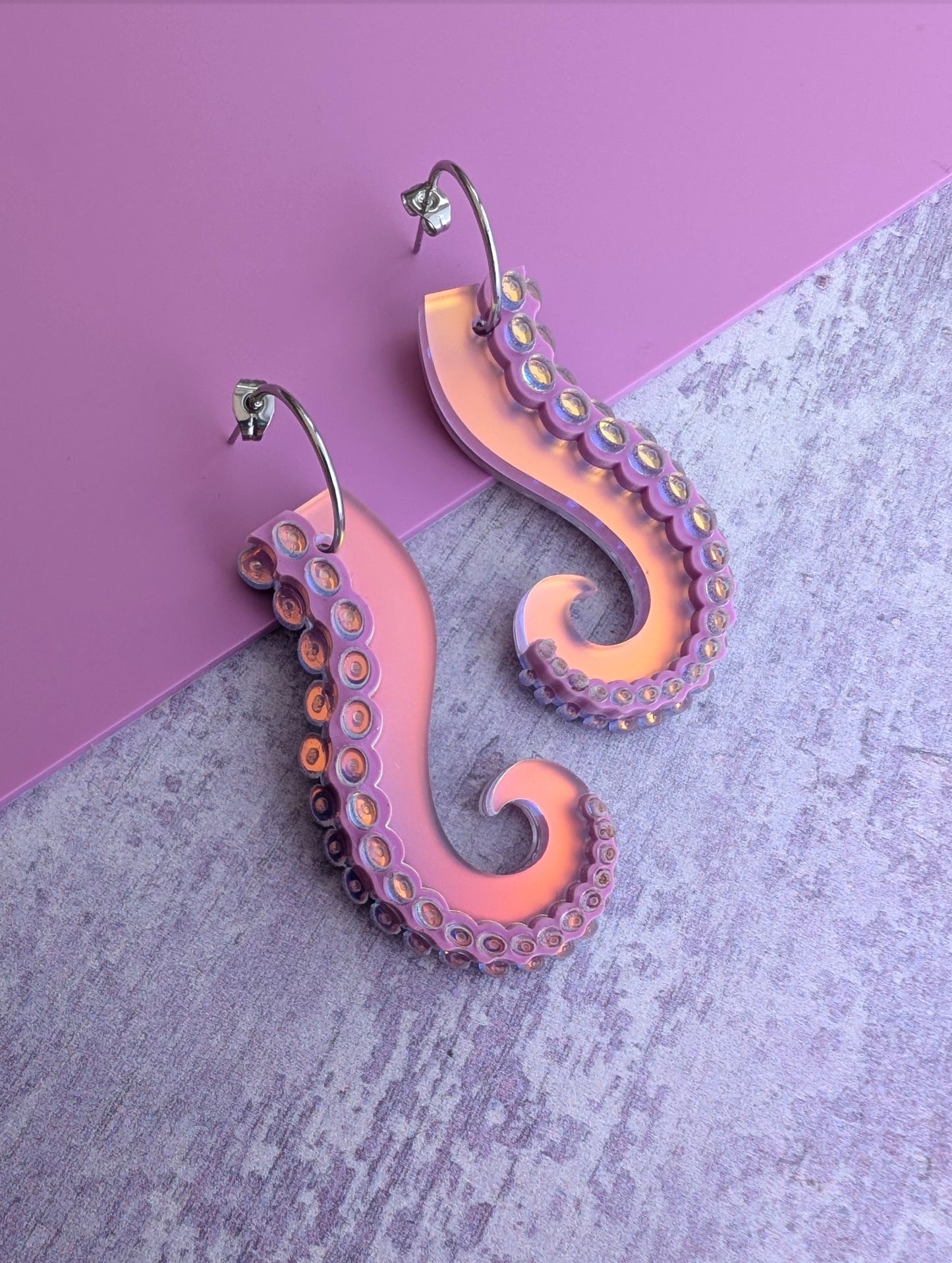 Iridescent lilac octopus tentacle earrings on a pink and gray background