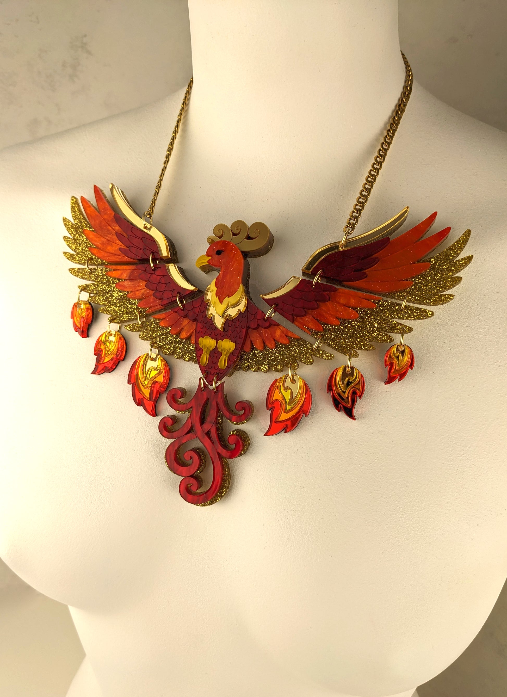 A striking acrylic phoenix necklace with yellow, red, and gold colors, displayed on a mannequin bust.