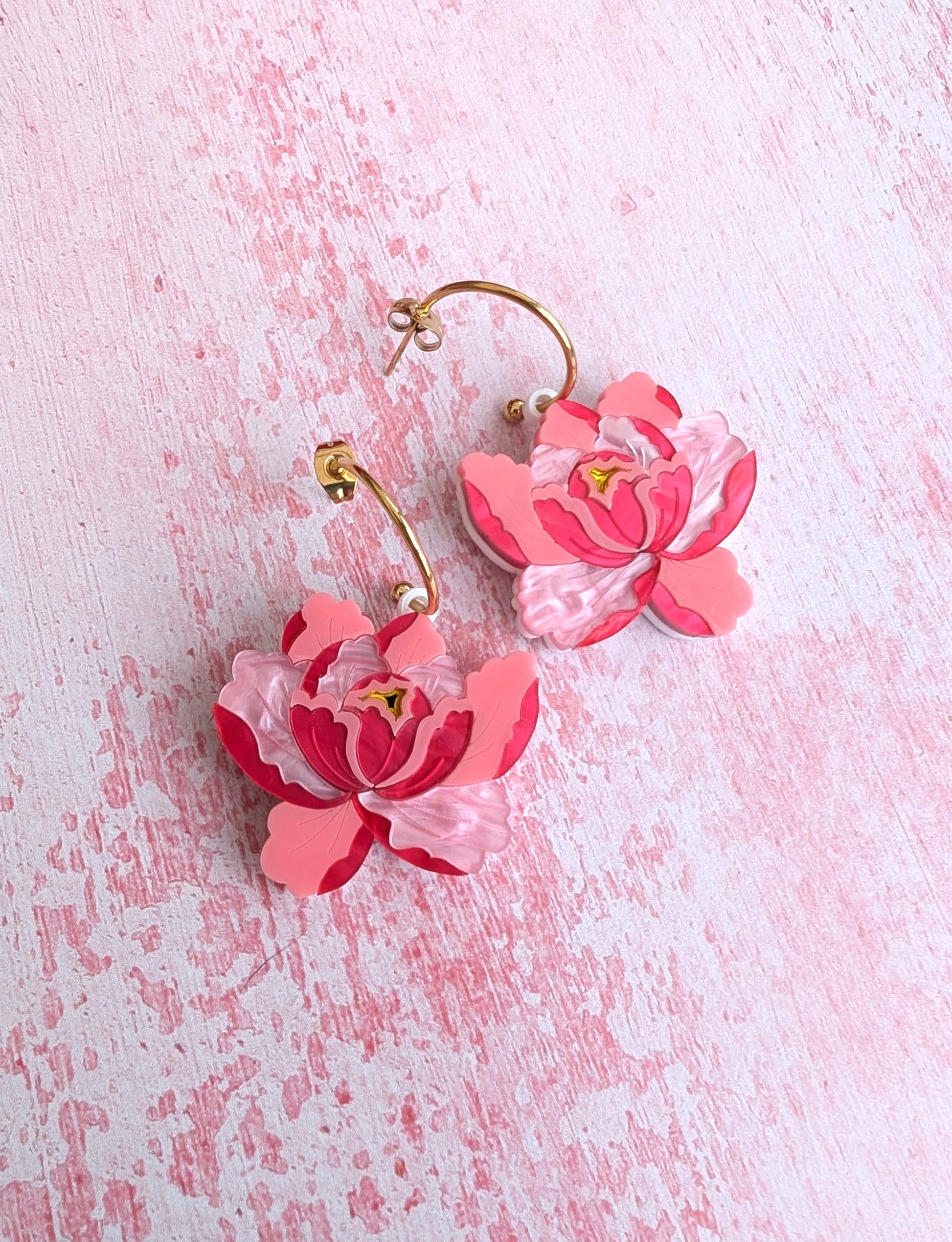 A pair of pink floral design earrings, resembling peony flowers, attached to the ear with a stud or hoops