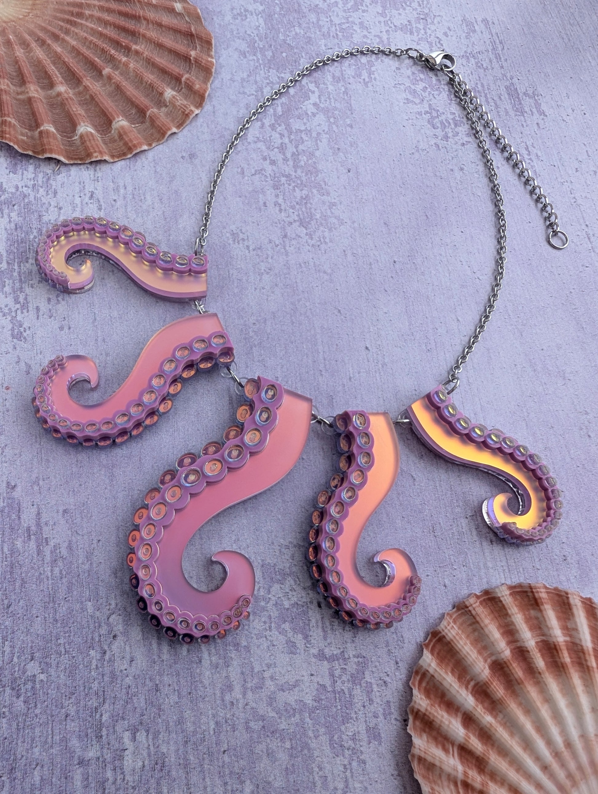 Laser cut sea witch themed acrylic necklace with octopus tentacle design on a textured surface with shells.