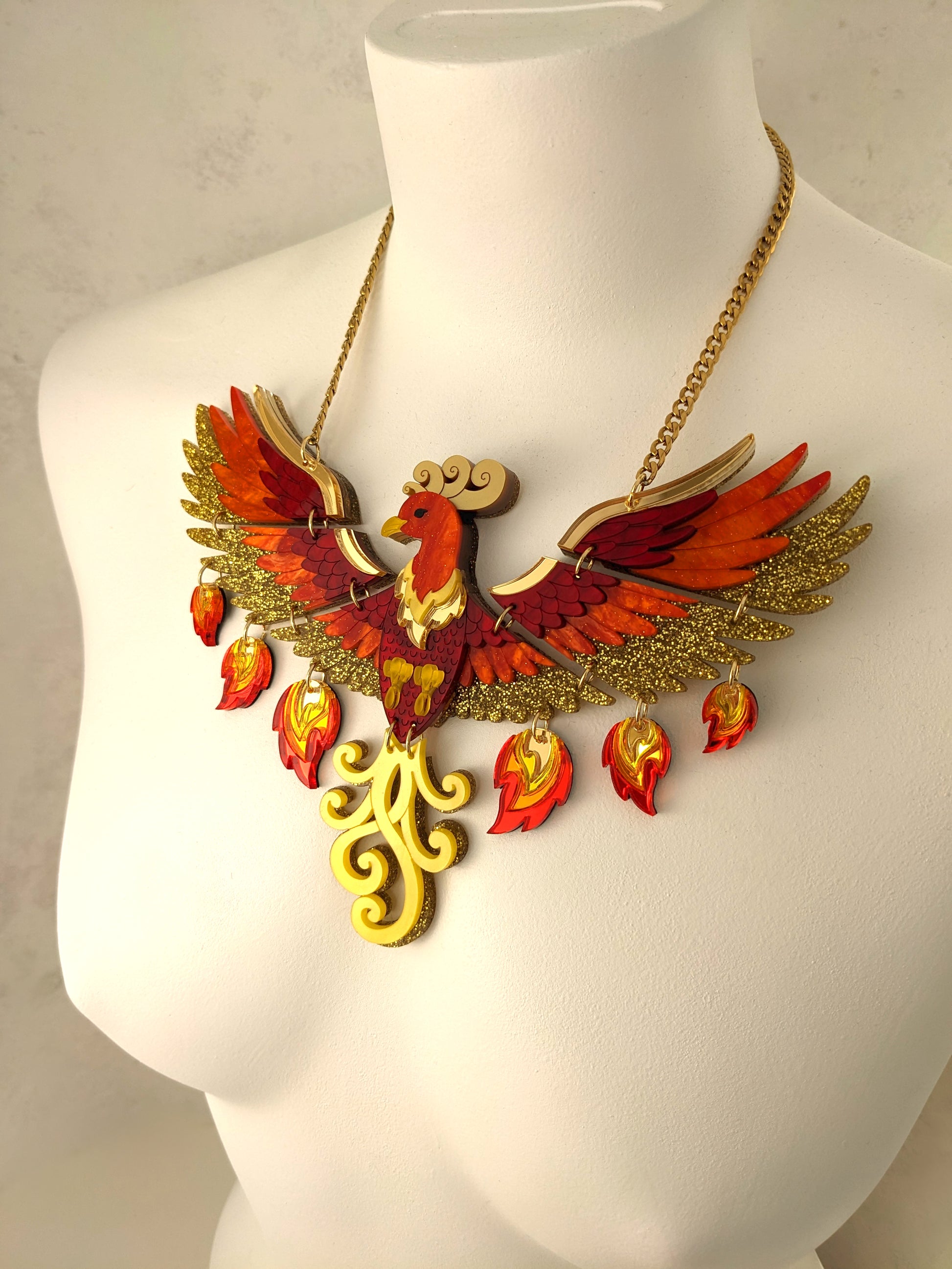 A striking acrylic phoenix necklace with yellow, red, and gold colors, displayed on a mannequin bust.