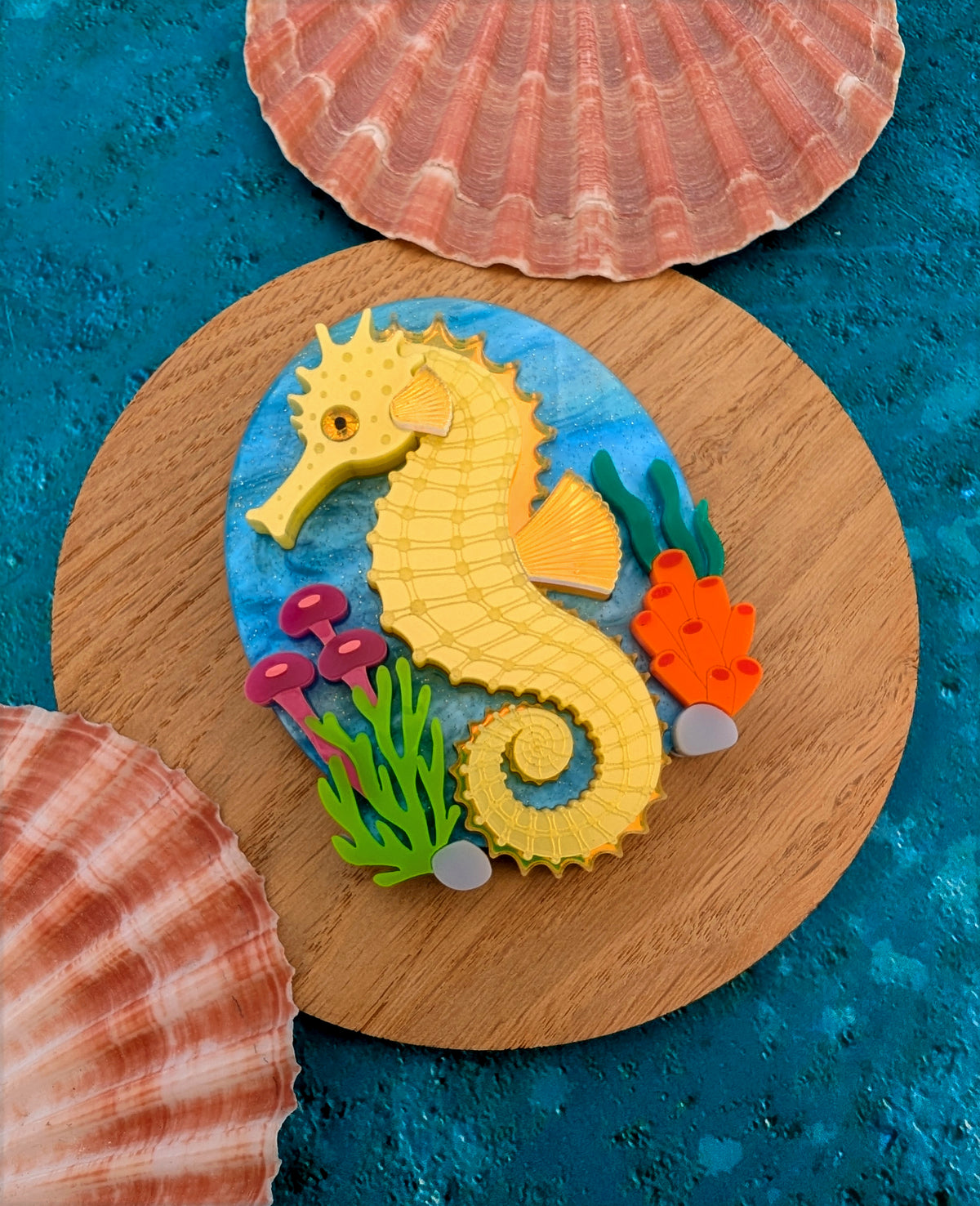 colourful laser cut acrylic seahorse brooch with a blue sea background and some underwater plants