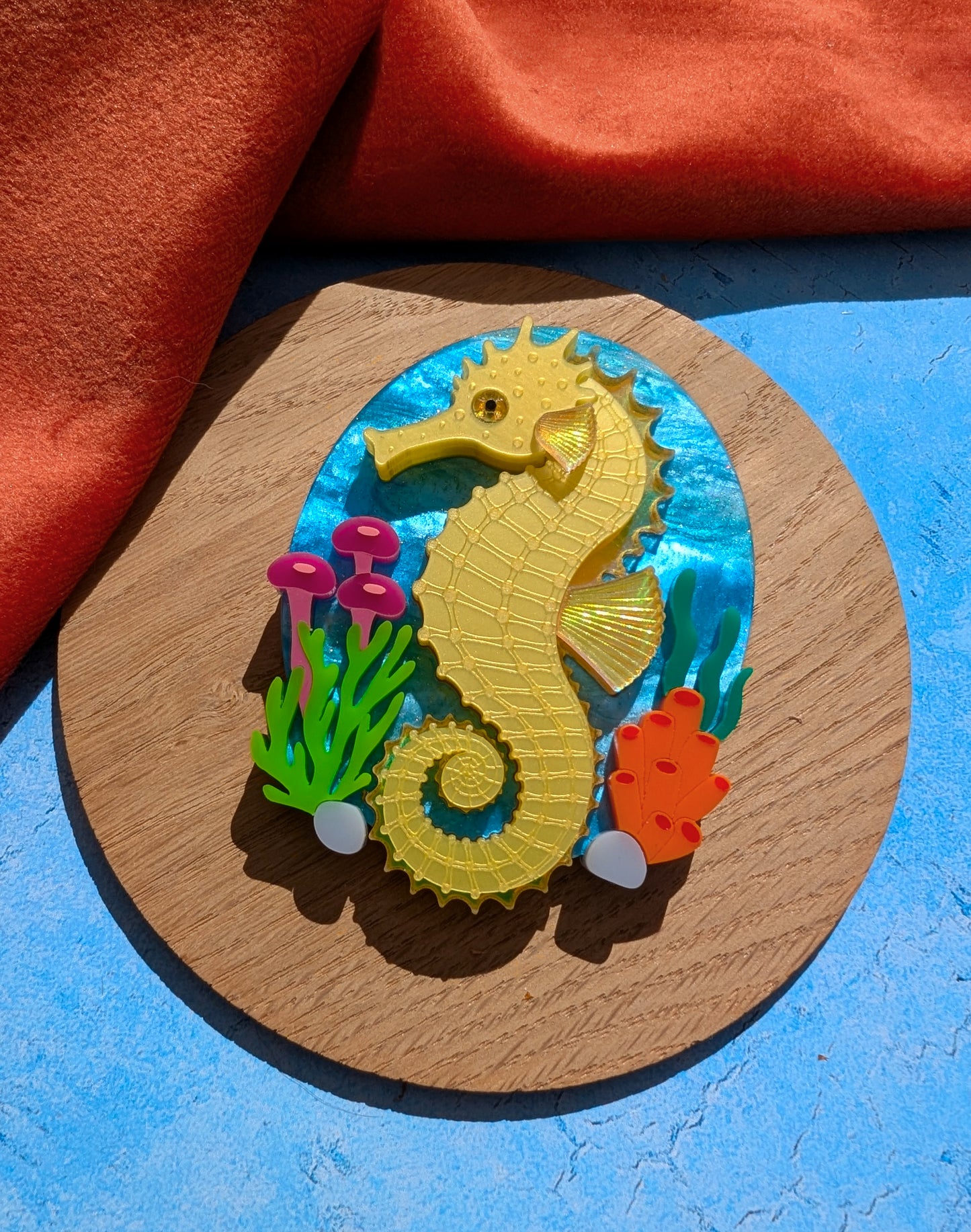 colourful laser cut acrylic seahorse brooch with a blue sea background and some underwater plants