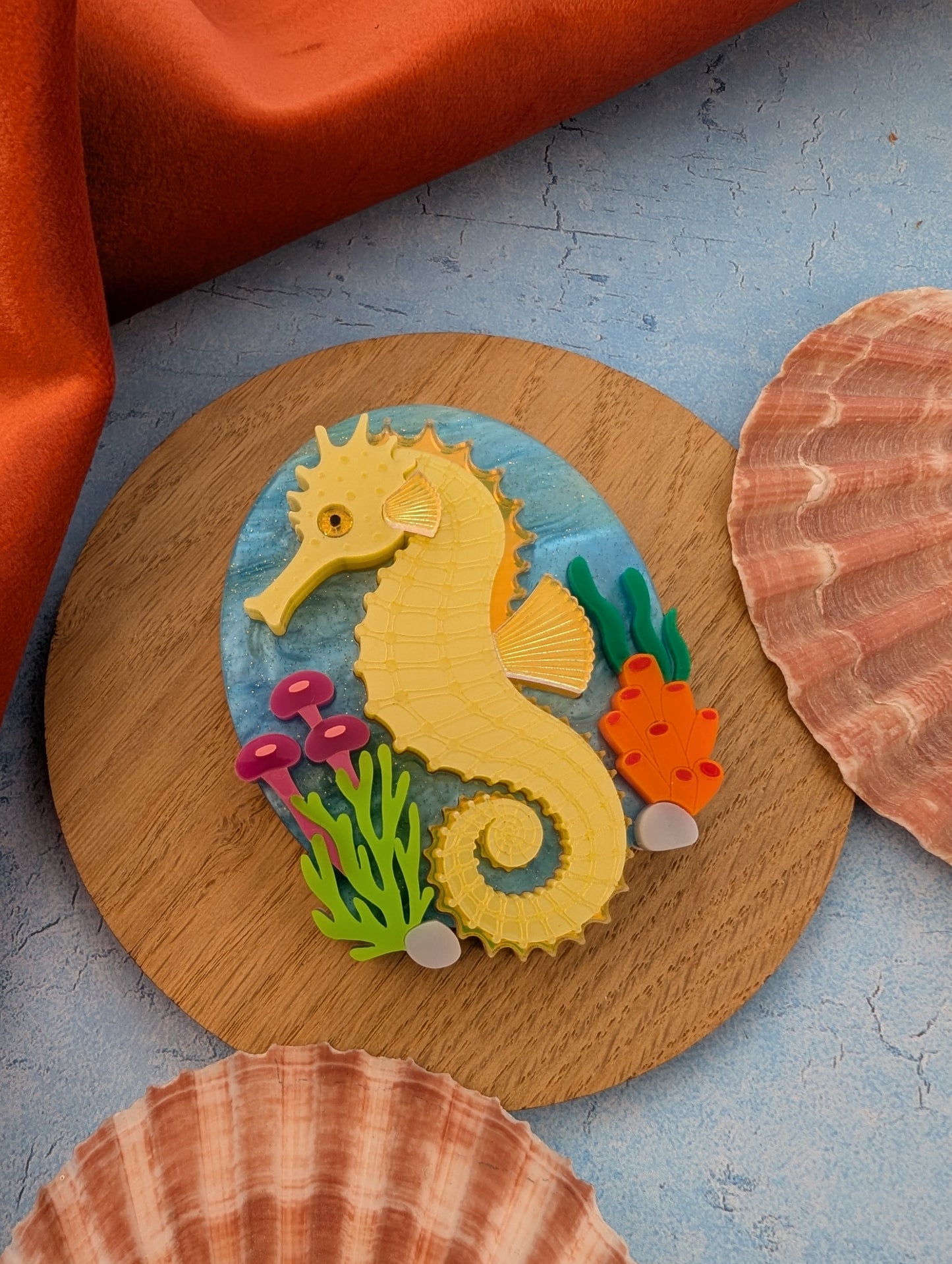 colourful laser cut acrylic seahorse brooch with a blue sea background and some underwater plants