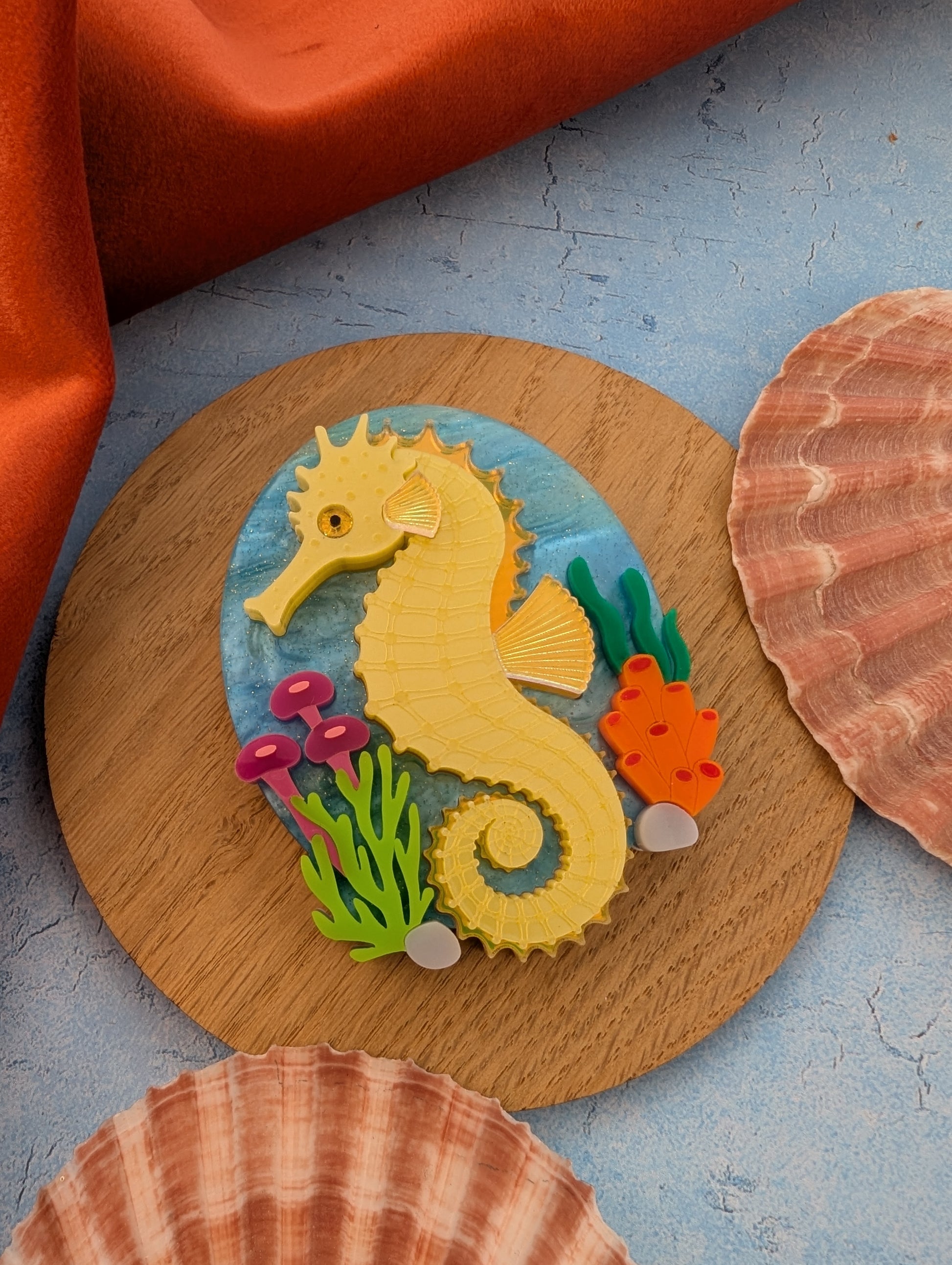 colourful laser cut acrylic seahorse brooch with a blue sea background and some underwater plants