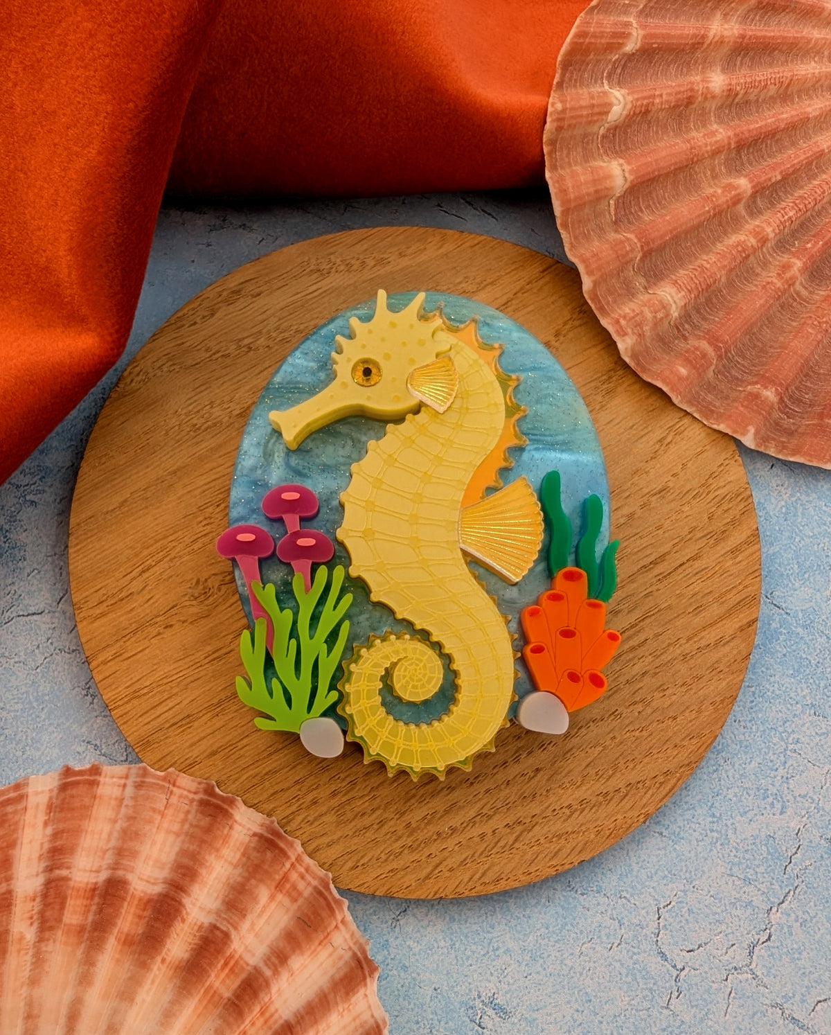 colourful laser cut acrylic seahorse brooch with a blue sea background and some underwater plants
