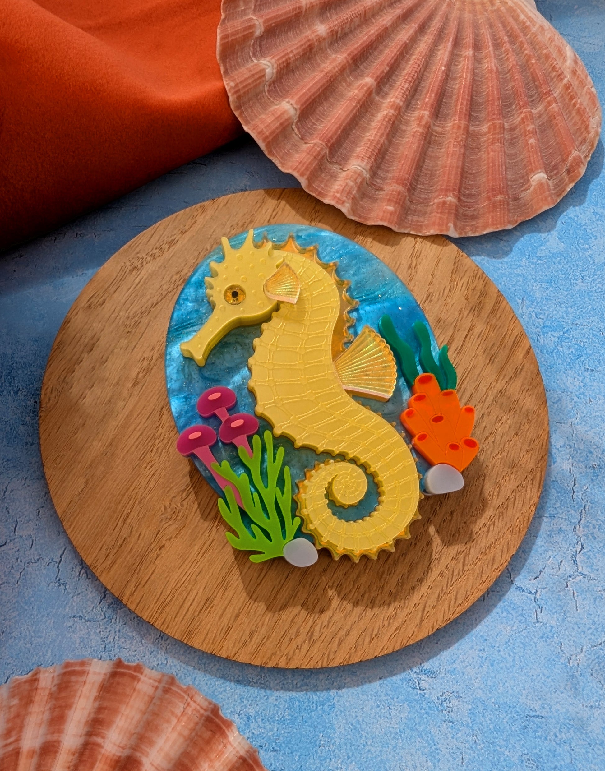 colourful laser cut acrylic seahorse brooch with a blue sea background and some underwater plants