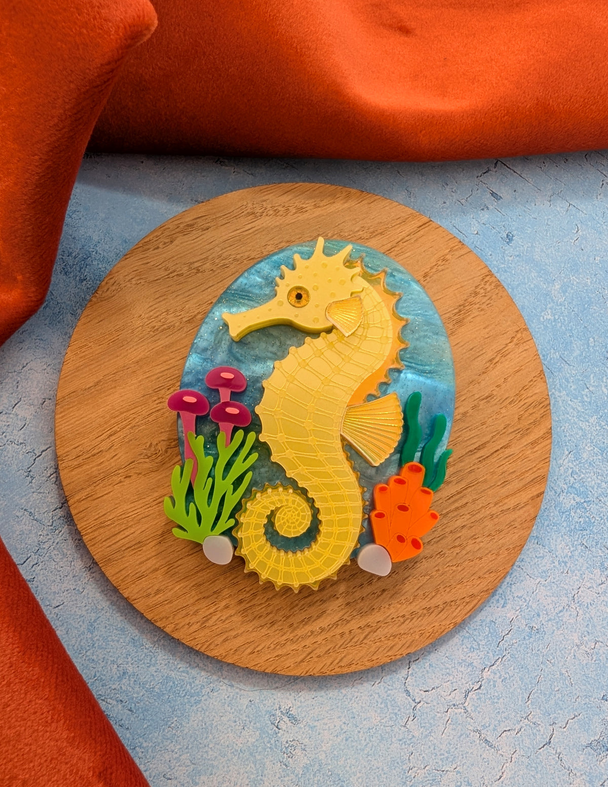 colourful laser cut acrylic seahorse brooch with a blue sea background and some underwater plants