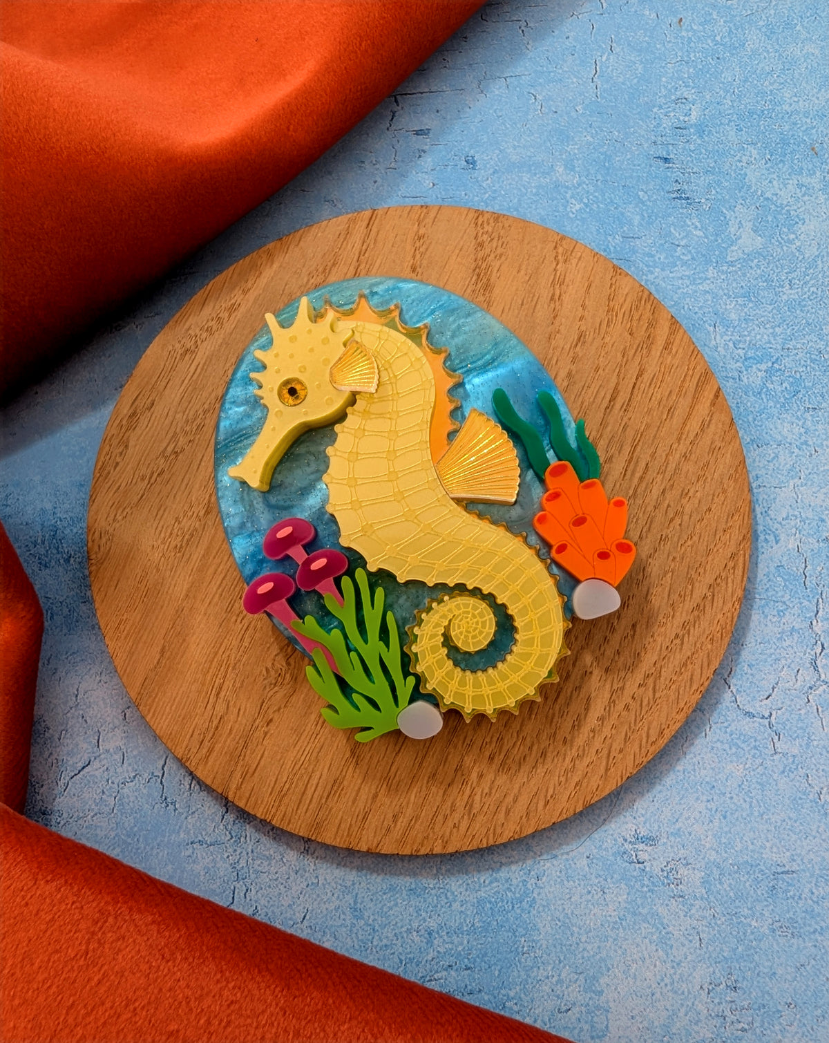 colourful laser cut acrylic seahorse brooch with a blue sea background and some underwater plants