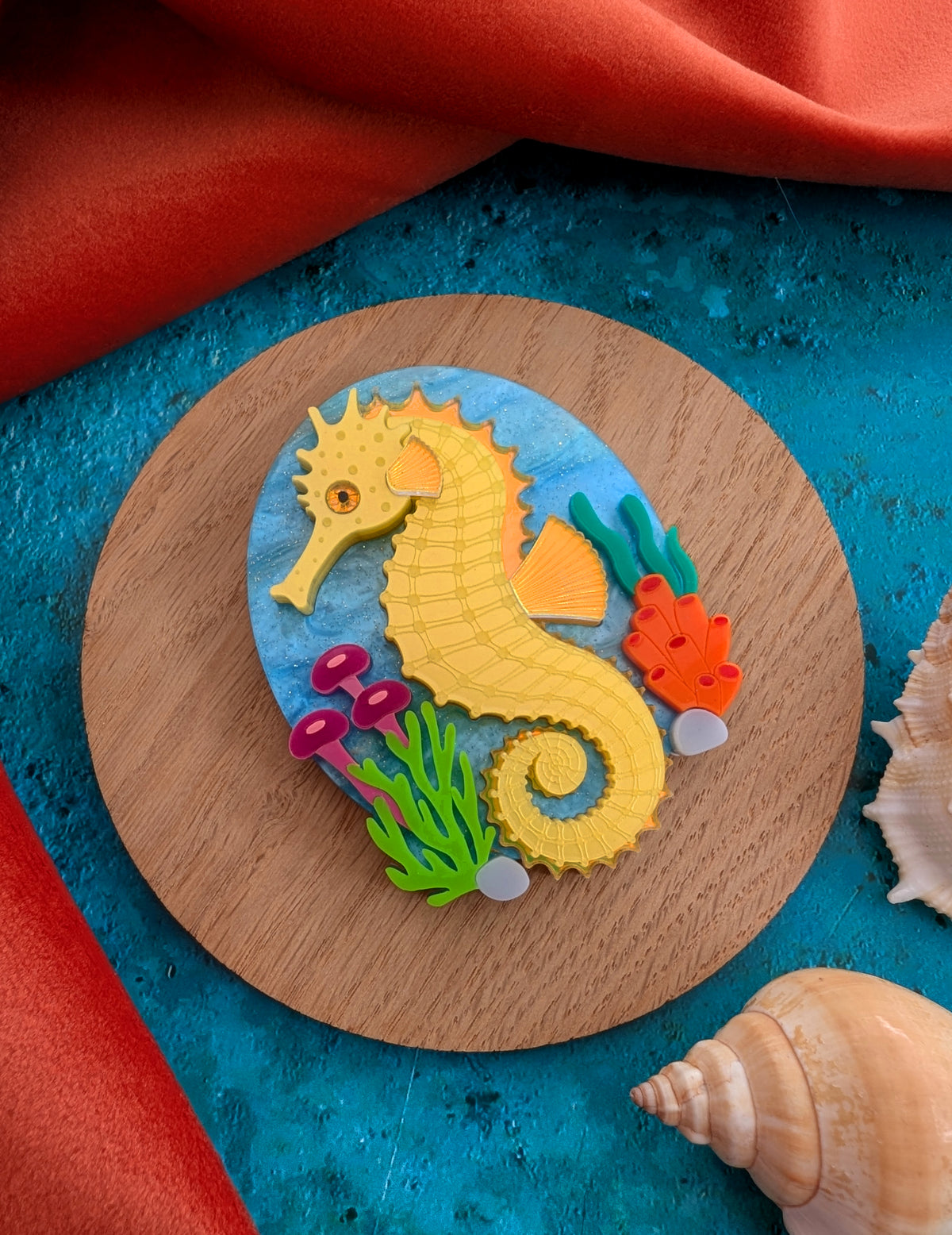 colourful laser cut acrylic seahorse brooch with a blue sea background and some underwater plants