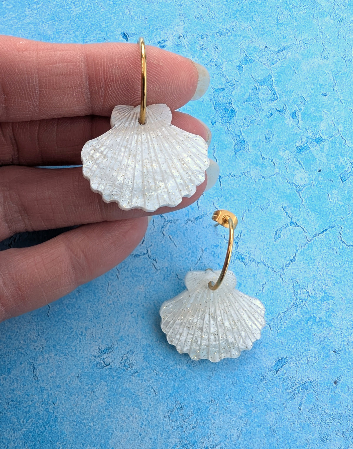 a pair of laser cut acrylic shell earrings on gold stainless steel hoops