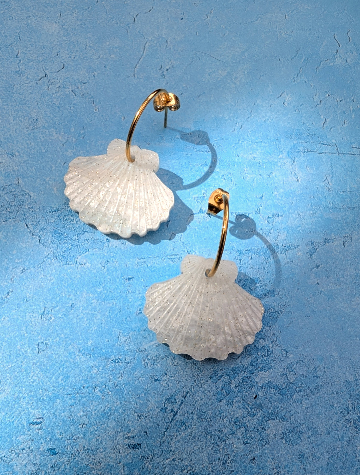 a pair of laser cut acrylic shell earrings on gold stainless steel hoops