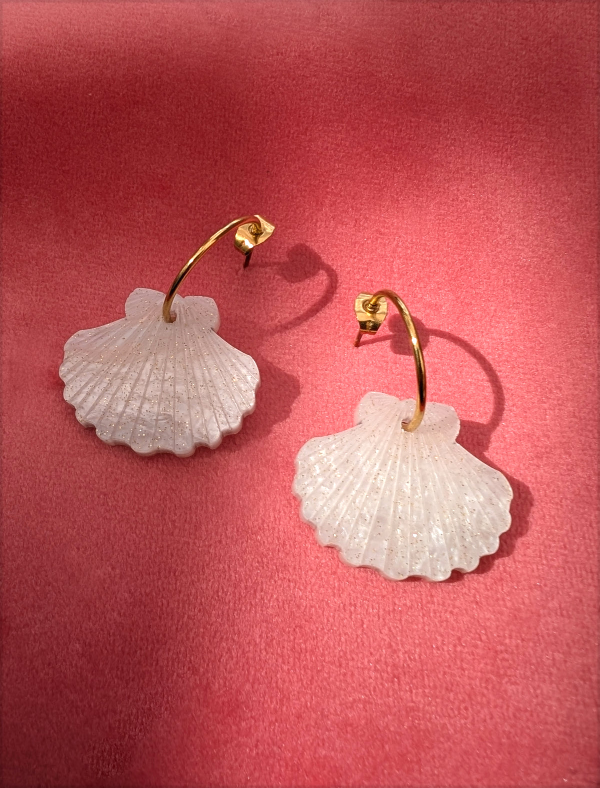 a pair of laser cut acrylic shell earrings on gold stainless steel hoops