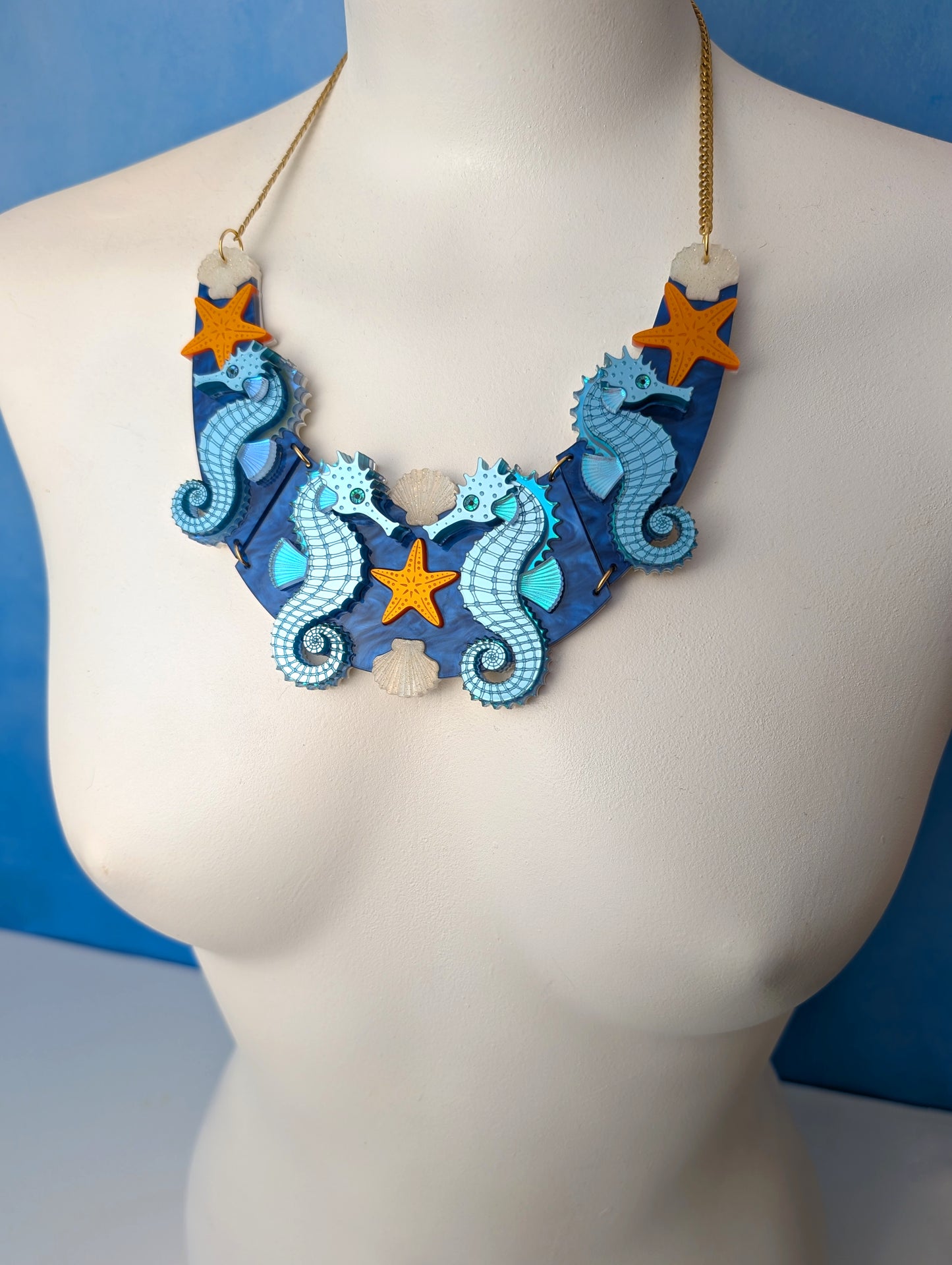a handmade laser cut acrylic necklace featuring blue seahorses, orange starfish and cream shells