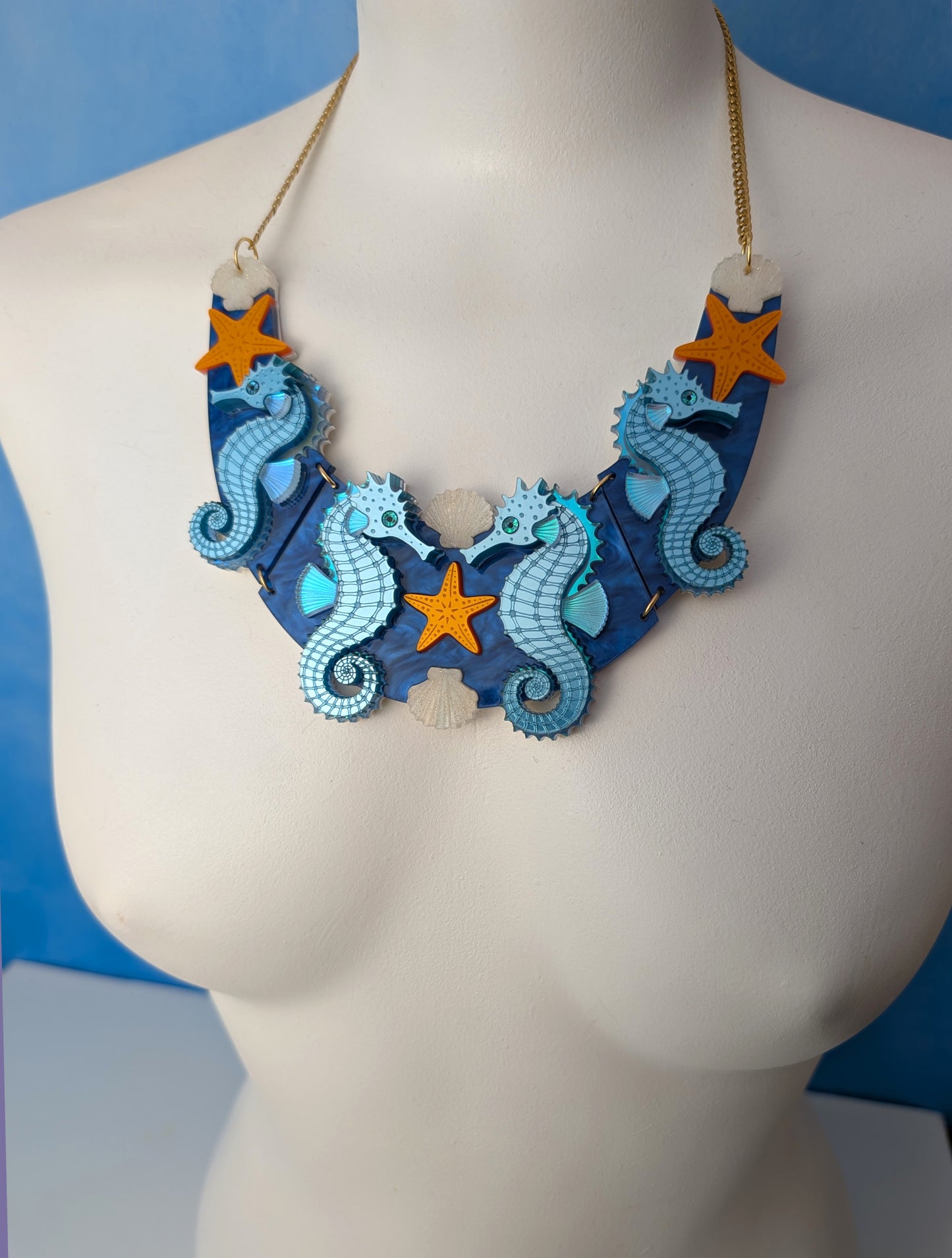 a handmade laser cut acrylic necklace featuring blue seahorses, orange starfish and cream shells