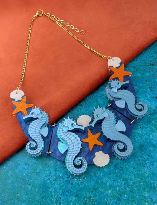 a handmade laser cut acrylic necklace featuring blue seahorses, orange starfish and cream shells