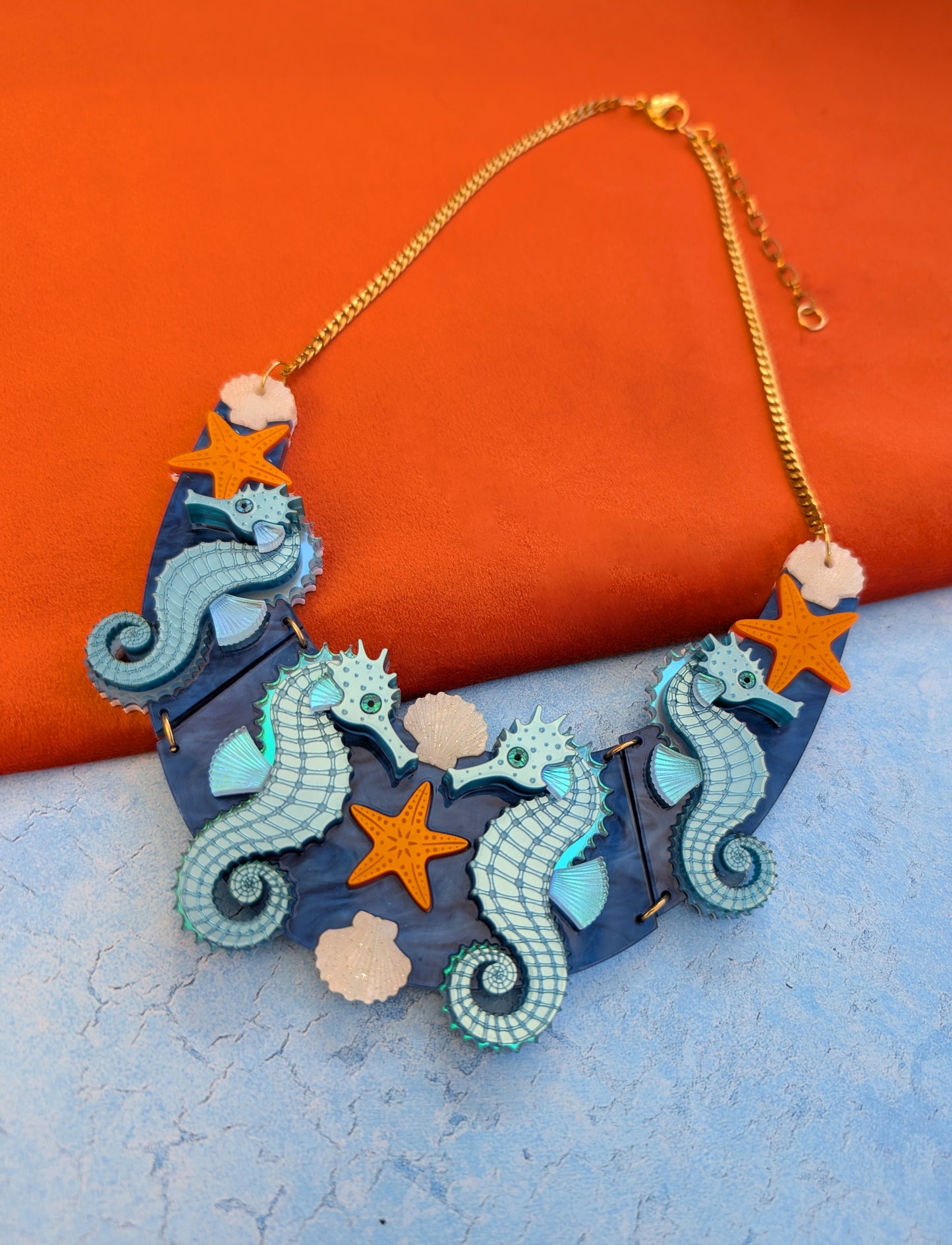 a handmade laser cut acrylic necklace featuring blue seahorses, orange starfish and cream shells