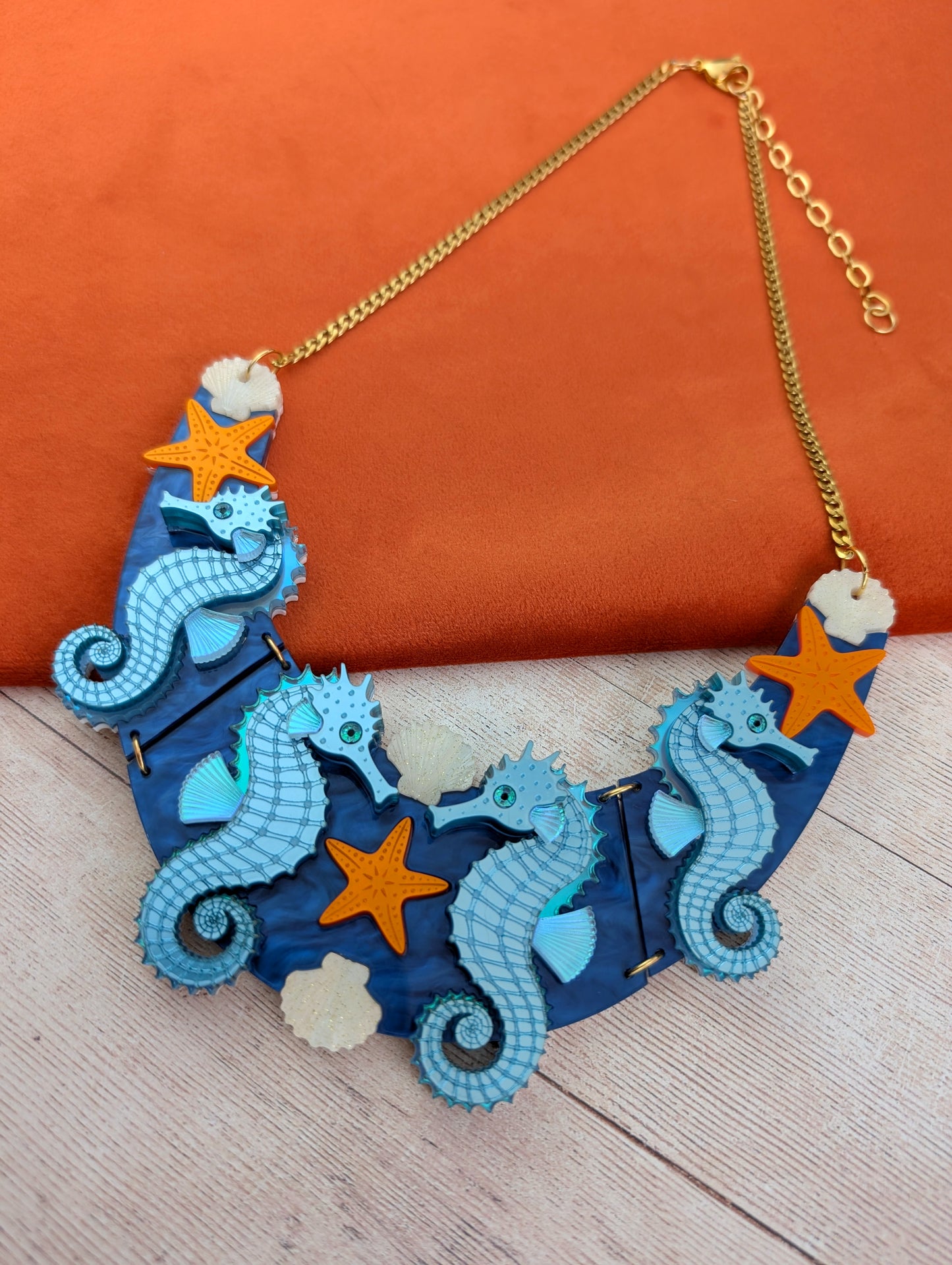 a handmade laser cut acrylic necklace featuring blue seahorses, orange starfish and cream shells