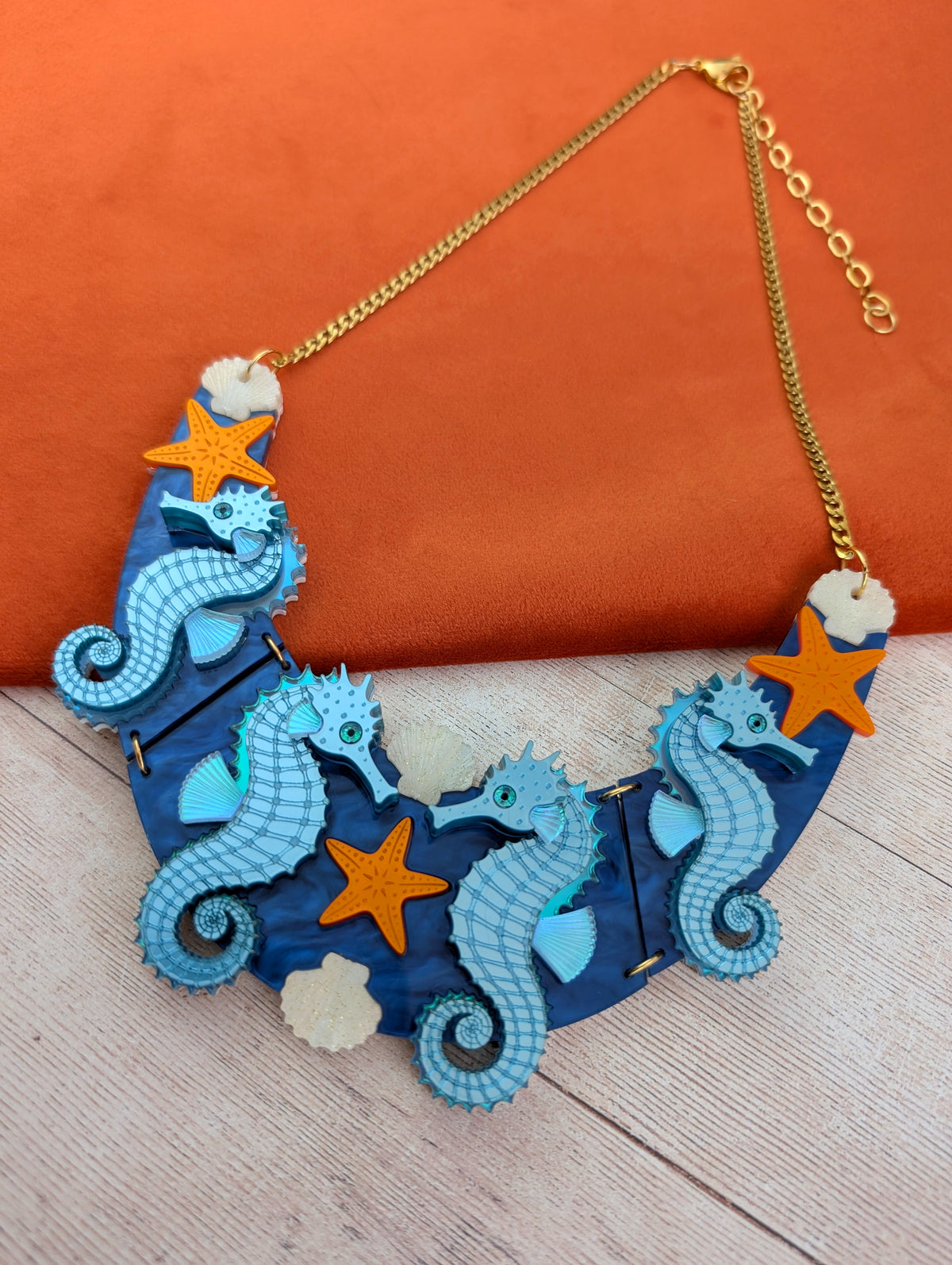 a handmade laser cut acrylic necklace featuring blue seahorses, orange starfish and cream shells