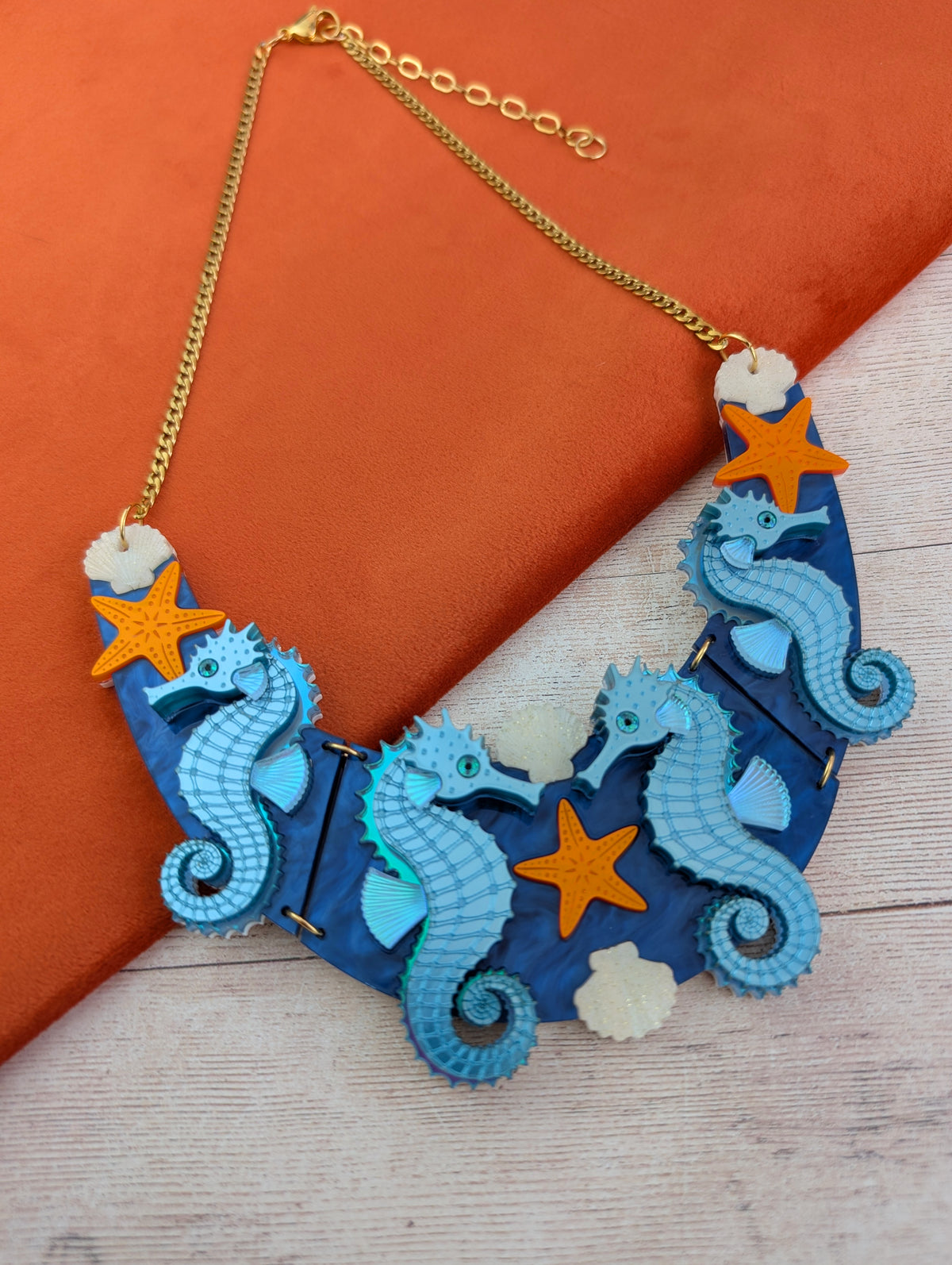 a handmade laser cut acrylic necklace featuring blue seahorses, orange starfish and cream shells