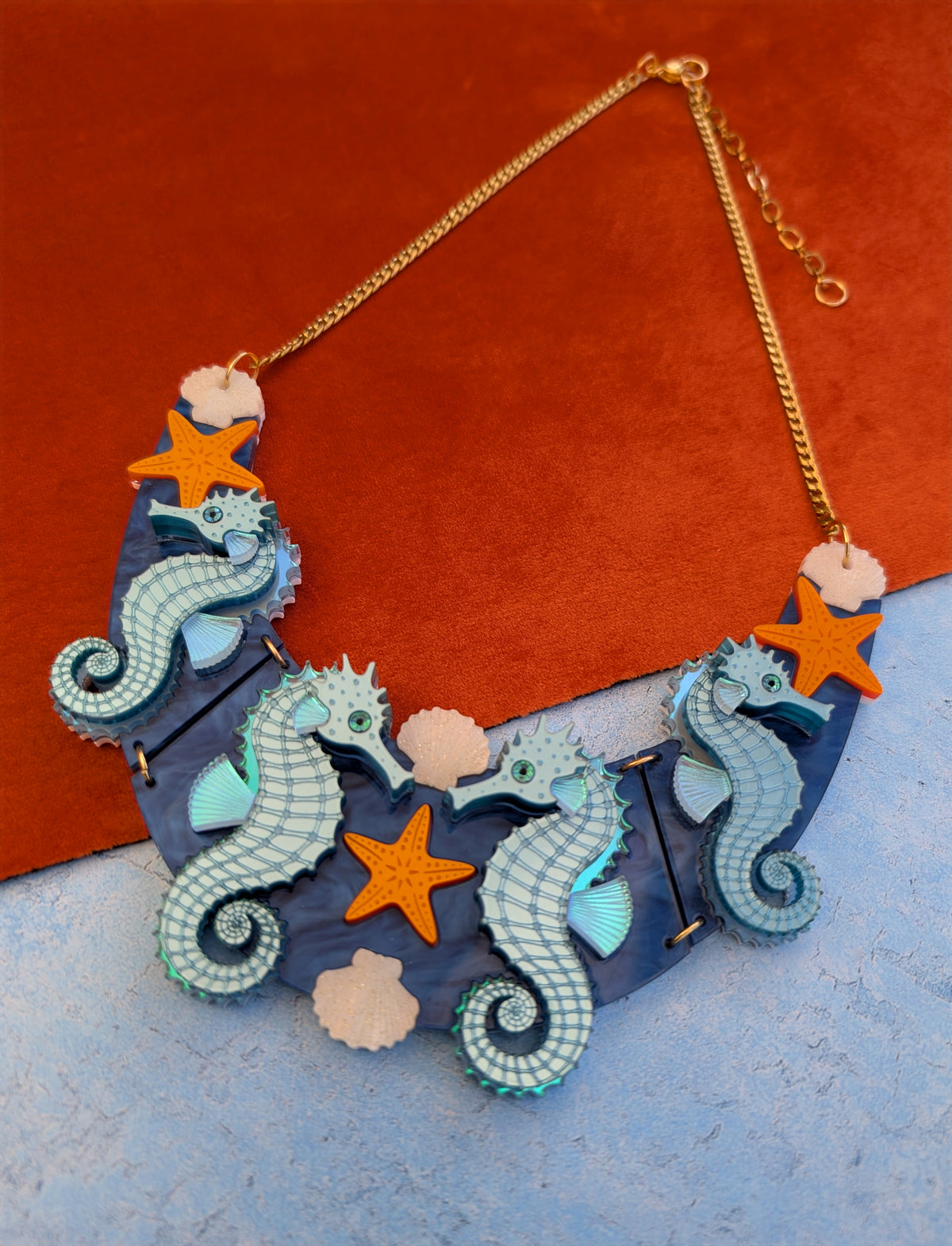 a handmade laser cut acrylic necklace featuring blue seahorses, orange starfish and cream shells