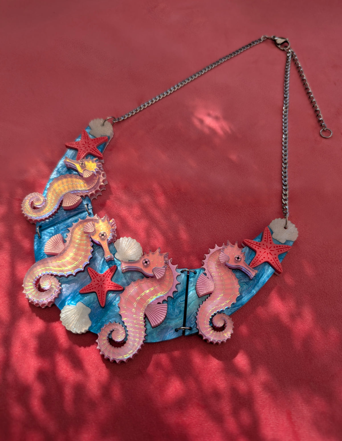 A handmade statement acrylic necklace featuring pink iridescent seahorses, coral starfish, and white seashells