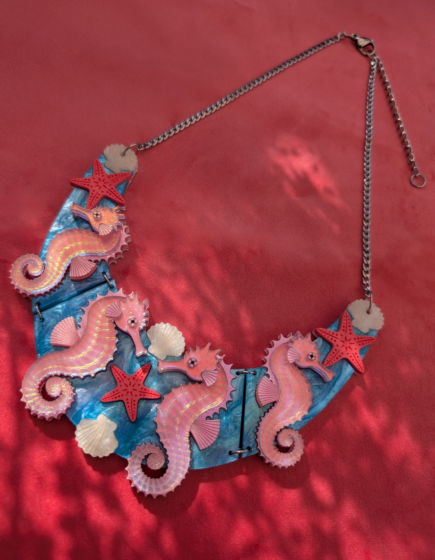 A handmade statement acrylic necklace featuring pink iridescent seahorses, coral starfish, and white seashells