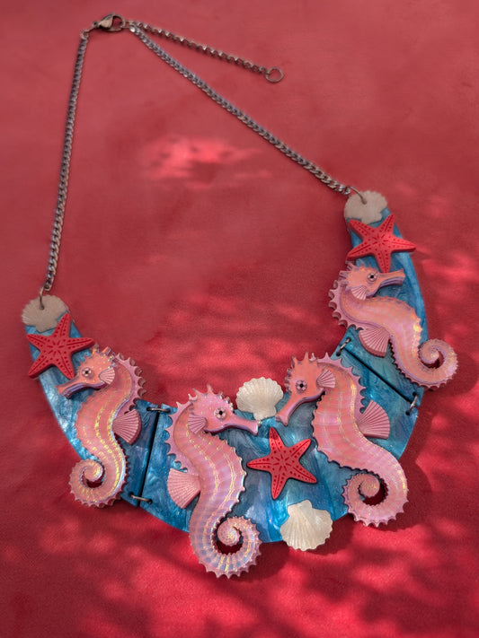 A handmade statement acrylic necklace featuring pink iridescent seahorses, coral starfish, and white seashells