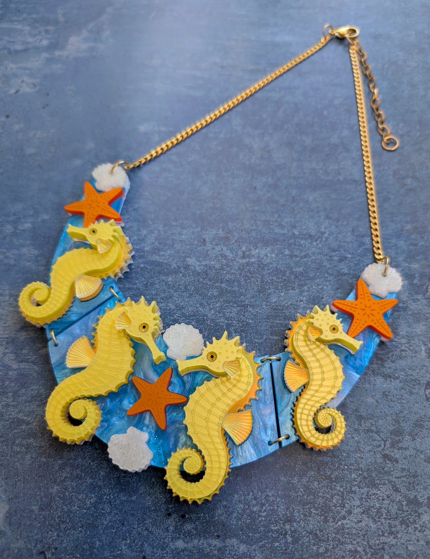 a handmade laser cut acrylic necklace featuring yellow seahorses, orange starfish and cream shells