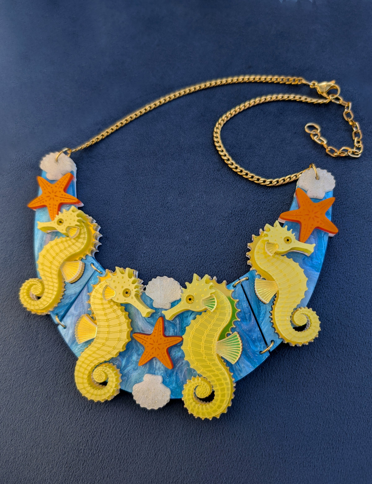 a handmade laser cut acrylic necklace featuring yellow seahorses, orange starfish and cream shells