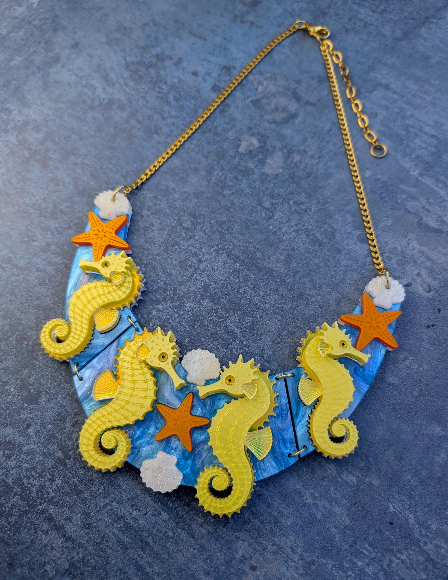 a handmade laser cut acrylic necklace featuring yellow seahorses, orange starfish and cream shells