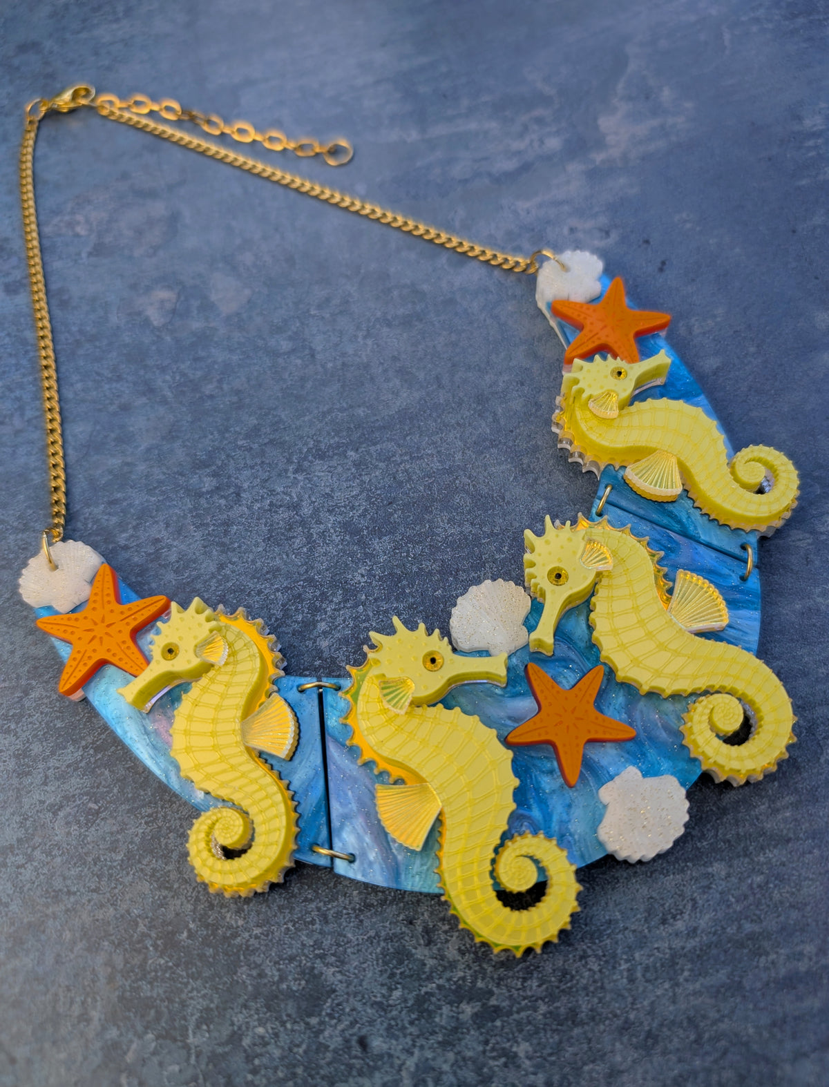 a handmade laser cut acrylic necklace featuring yellow seahorses, orange starfish and cream shells