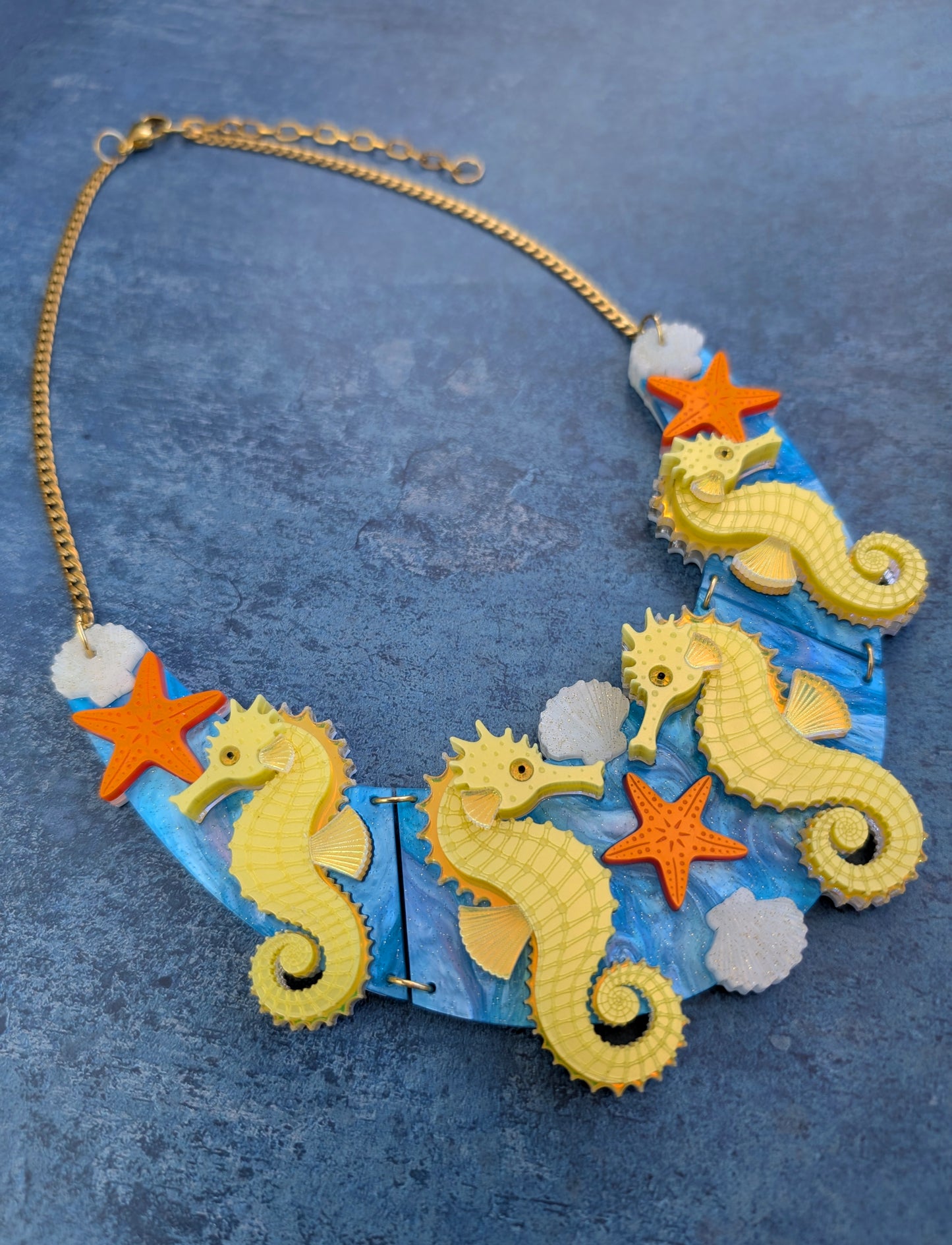 a handmade laser cut acrylic necklace featuring yellow seahorses, orange starfish and cream shells